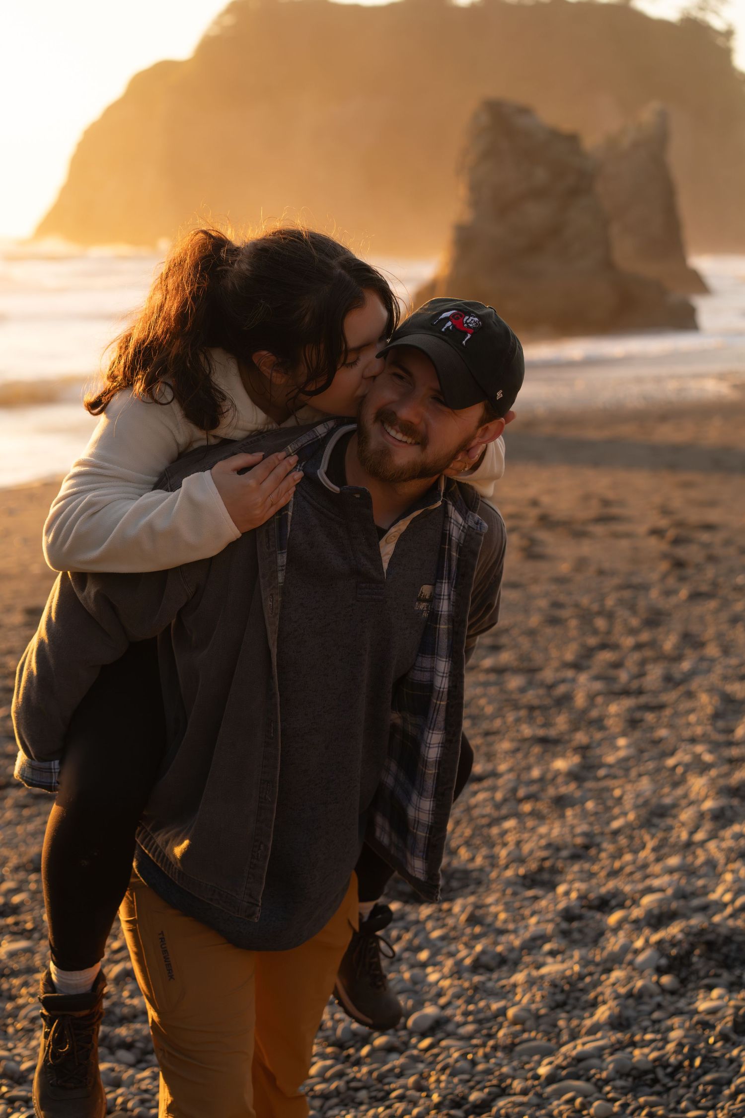 A couple embraces on a rocky beach at sunset with golden light illuminating the coastline. captured by Savvy Photography - proposal photo