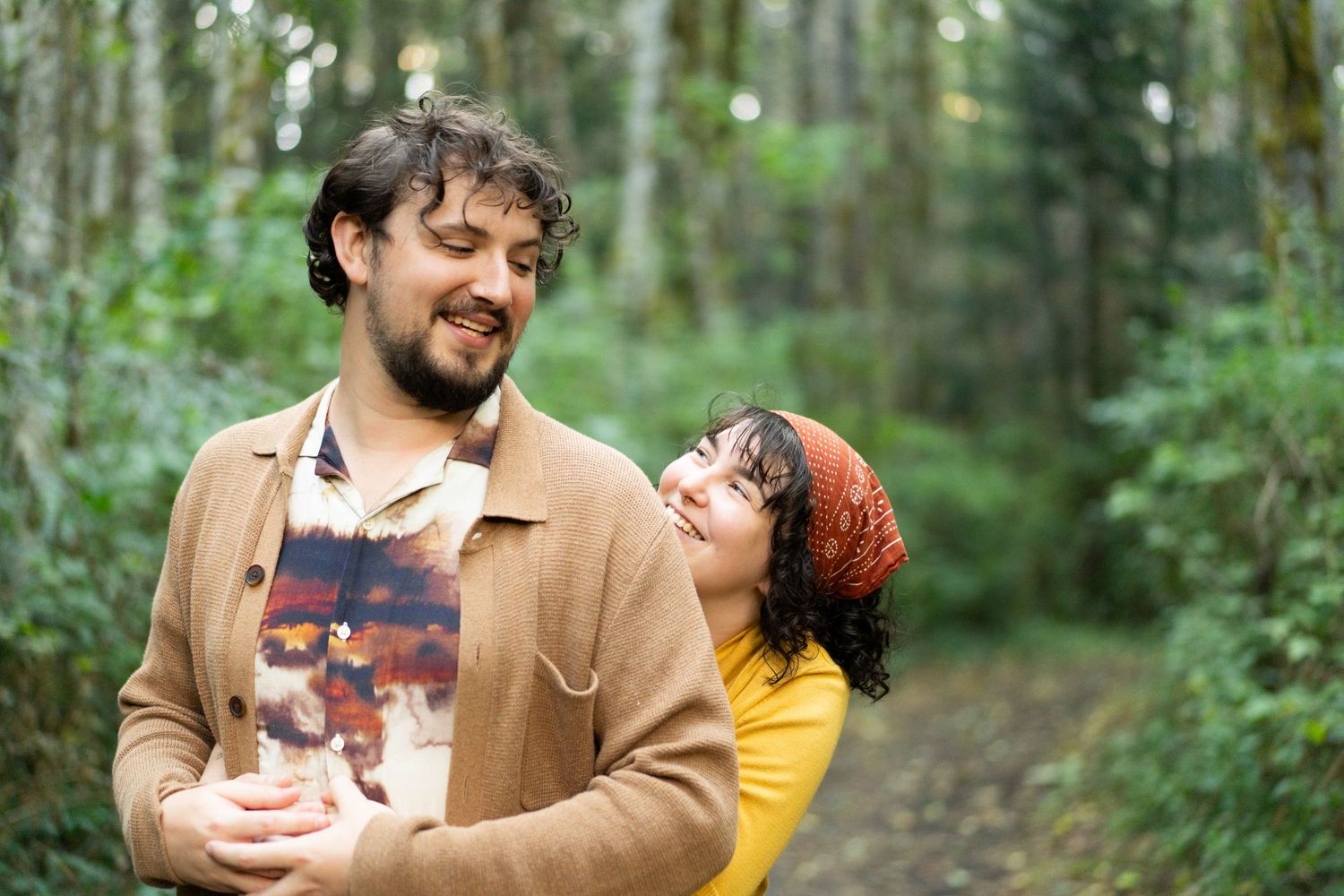 A couple shares a tender moment while walking through a lush green forest path. captured by Savvy Photography - Seattle Wedding Photographer
