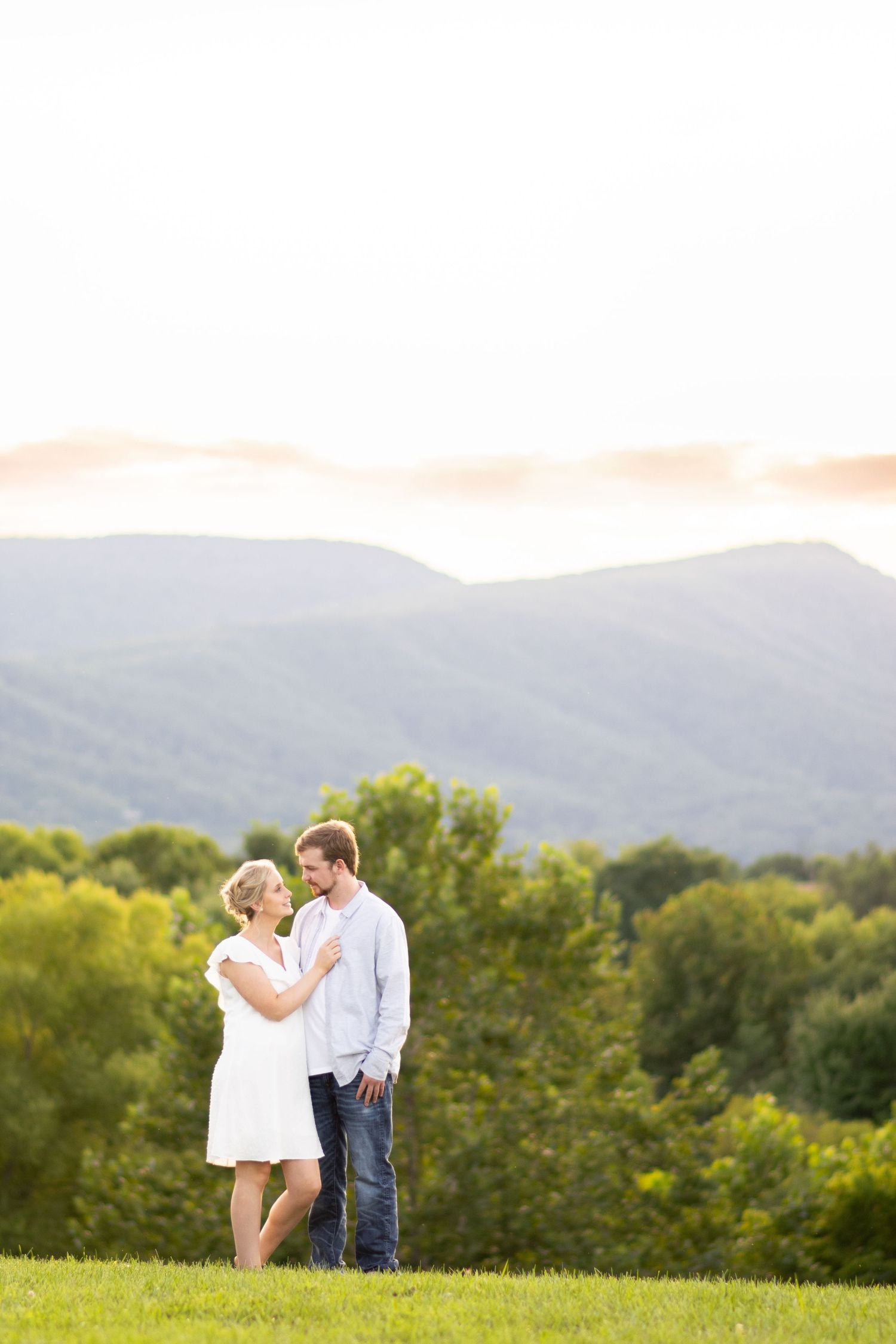 Couple sharing a romantic moment on a green hillside with scenic mountain views in the background.
