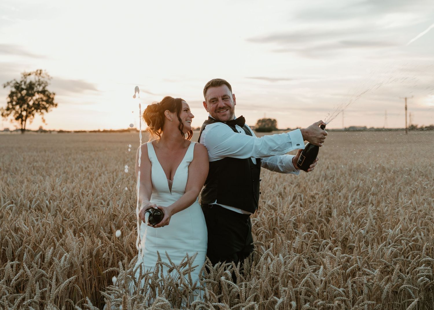 A couple poses romantically in a golden wheat field at sunset, creating a dreamy silhouette against the warm sky.