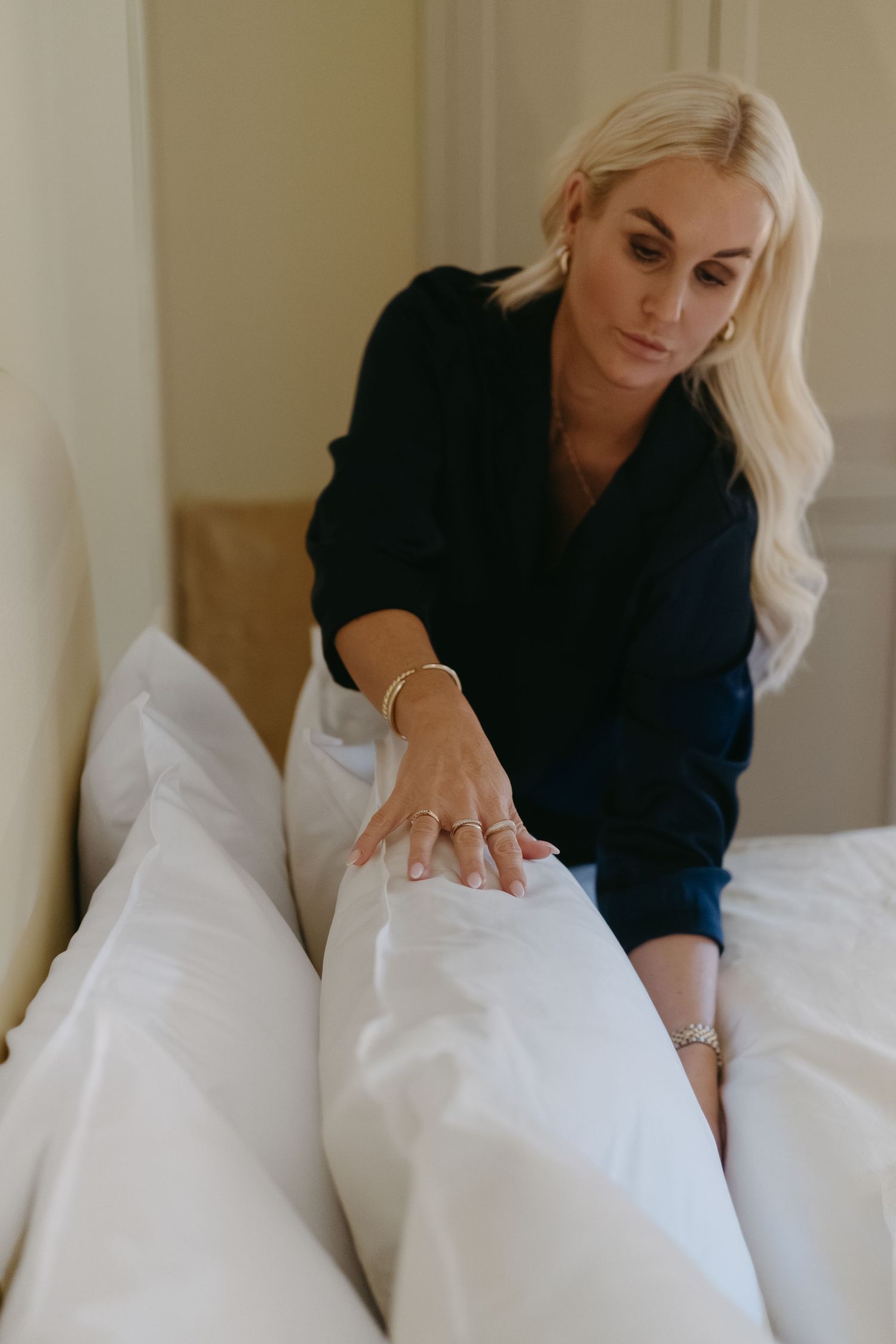 woman fluffing pillows in bed while being captured by lifestyle brand photographer in Stockholm