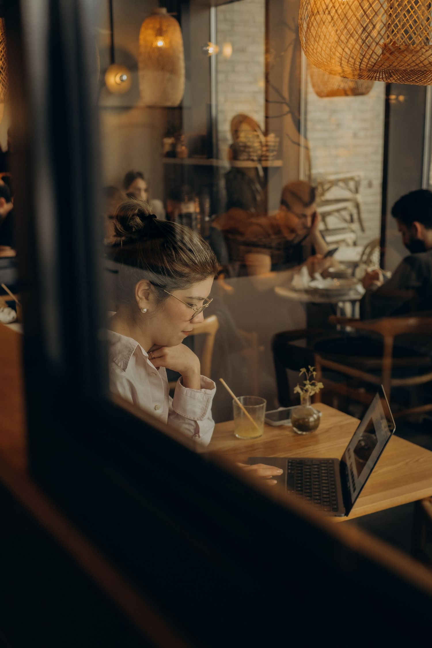 a woman sitting in a coffee shop looking into her laptop while being captured through a window by event photographer in Stockholm