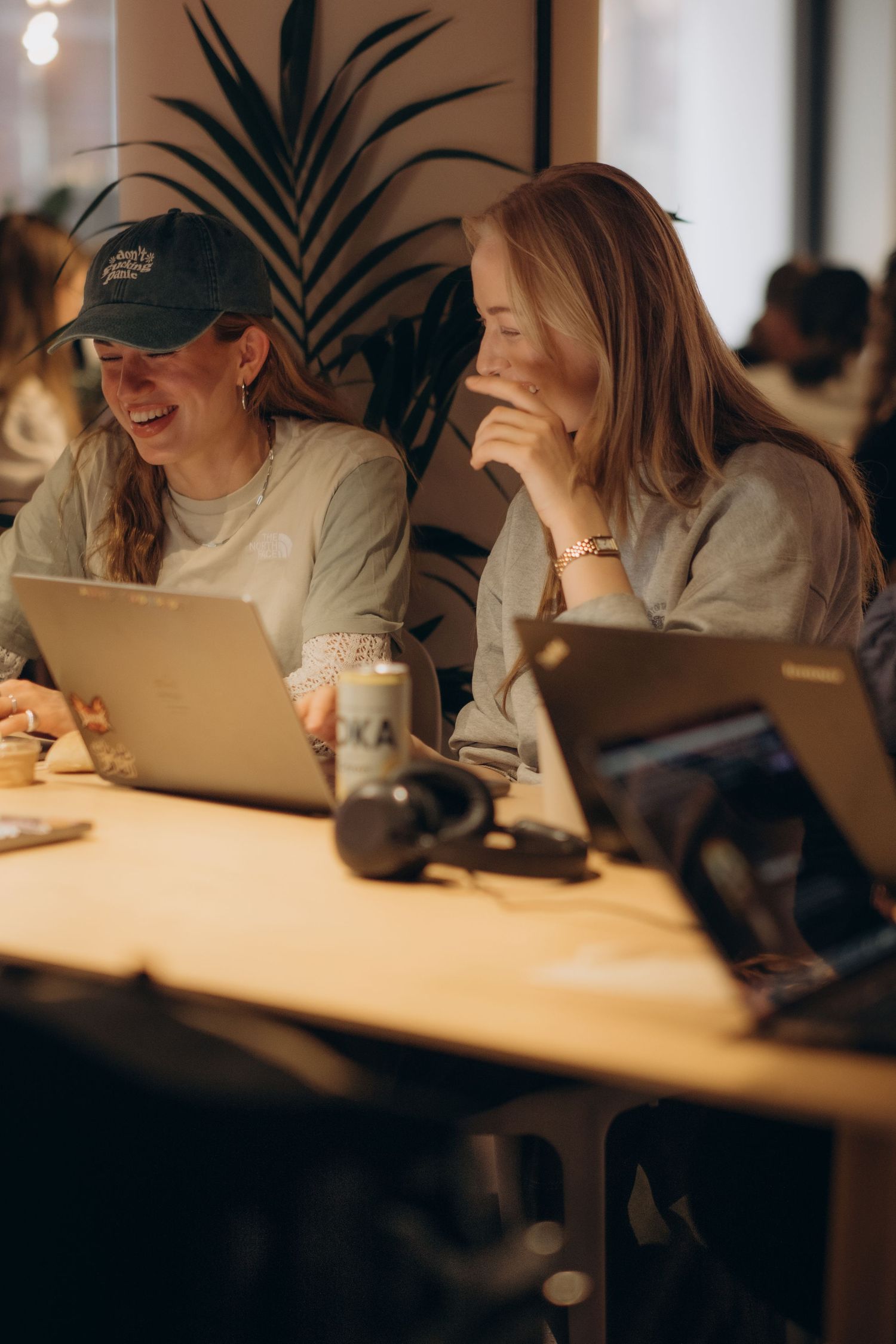 two women sitting bind their computers laughing while being captured by professional conference photographer in Stockholm