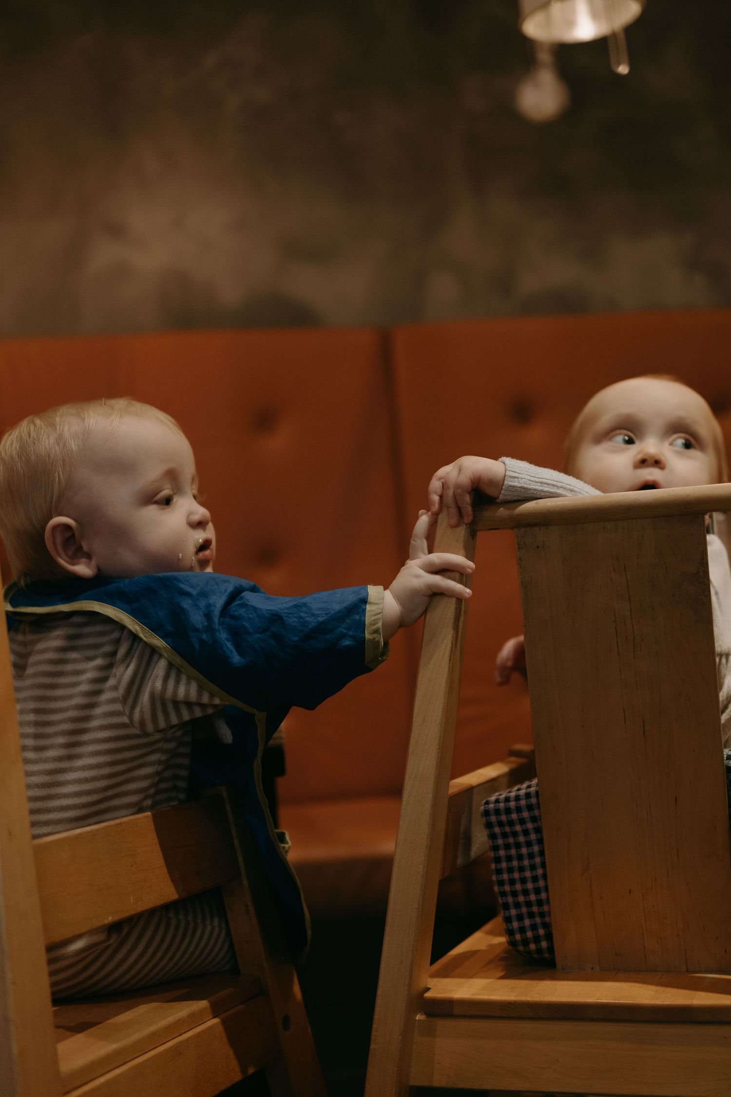 two babies sitting in high chairs in a Stockholm café touching each other with their fingers while being captured by Stockholm photographer