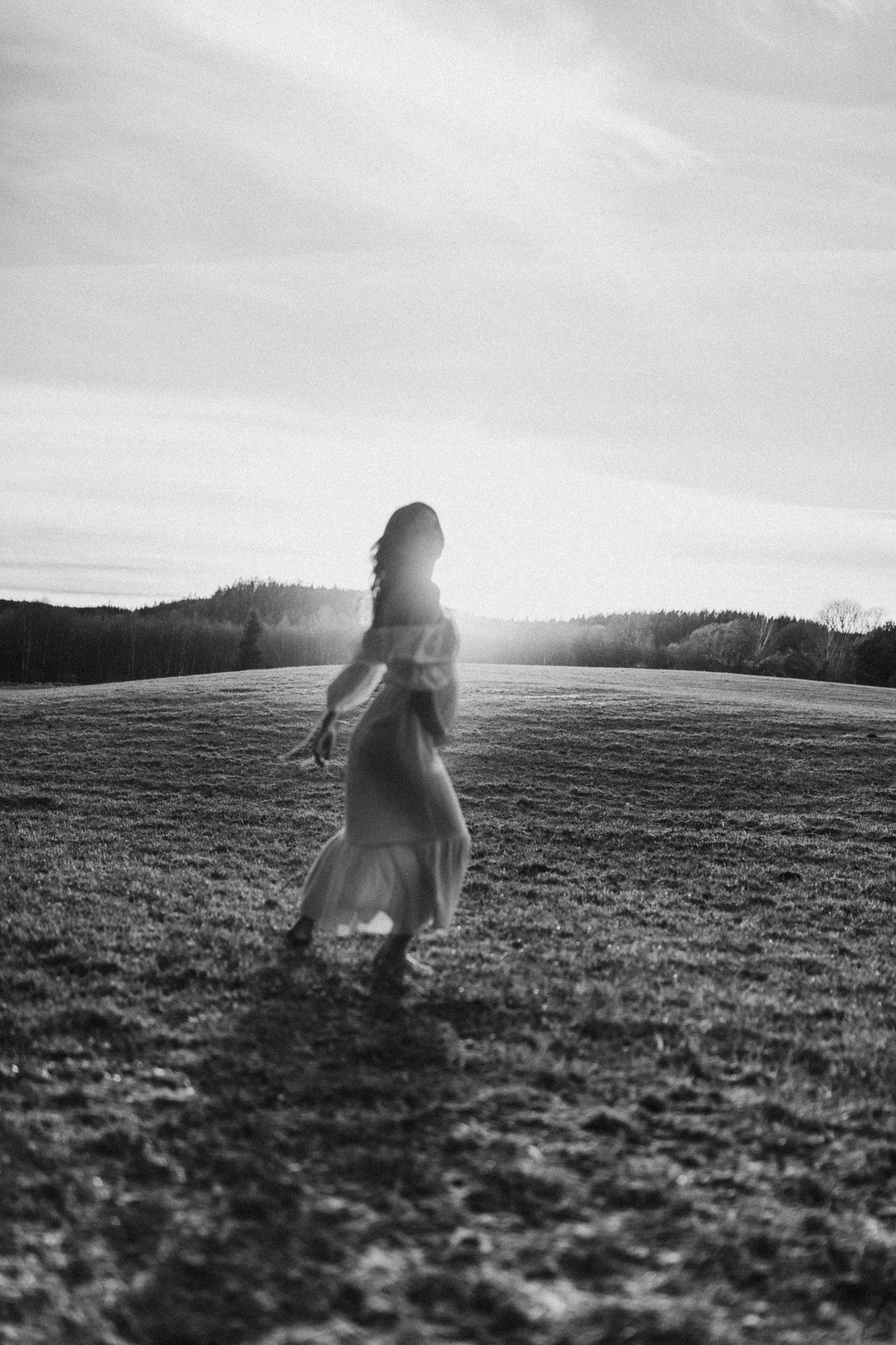 Black and white photo of a silhouetted figure running through a sunlit field at sunset.