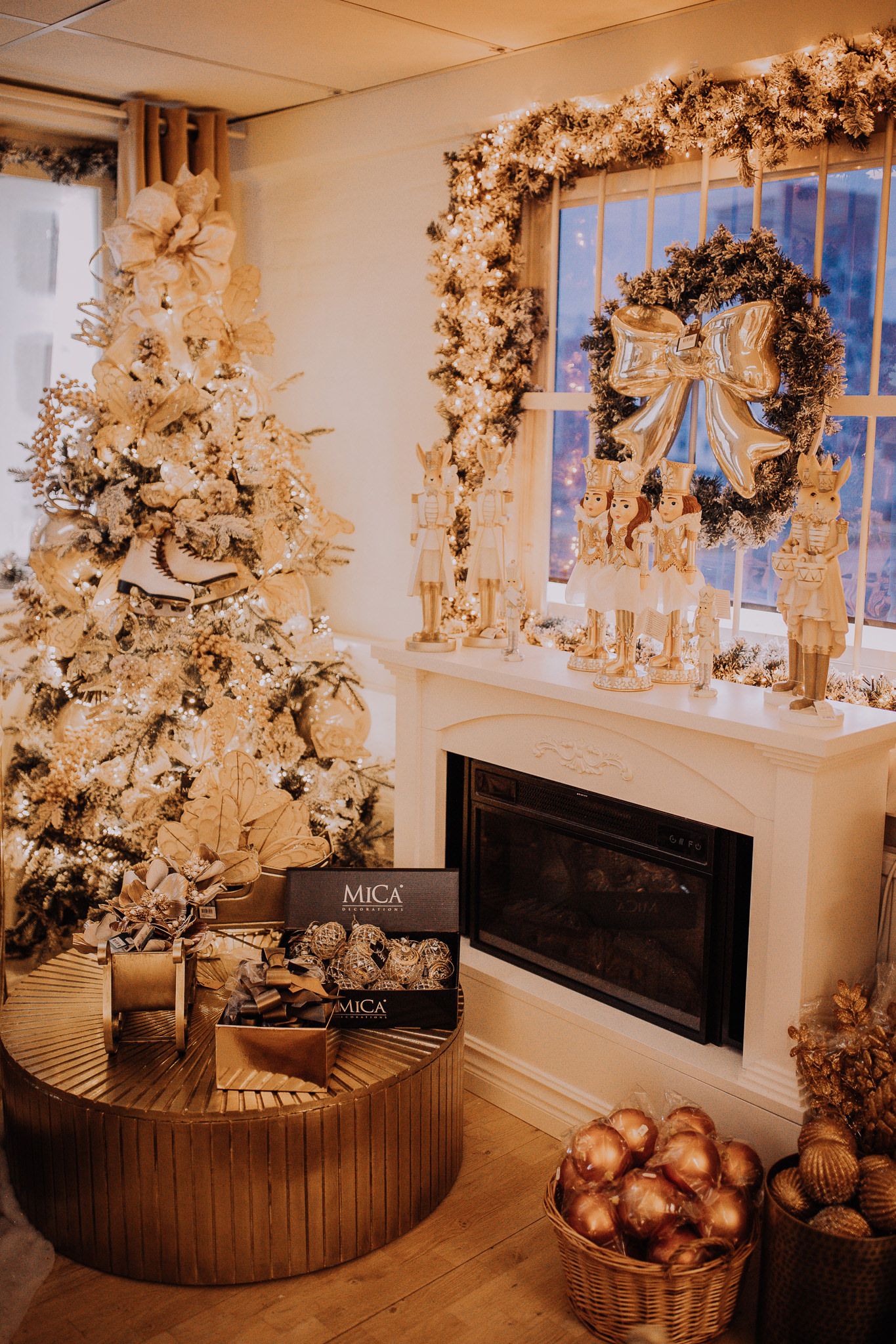 Gold Christmas tree and wreath decor with MICA gifts by a white fireplace in an elegant holiday room setting.