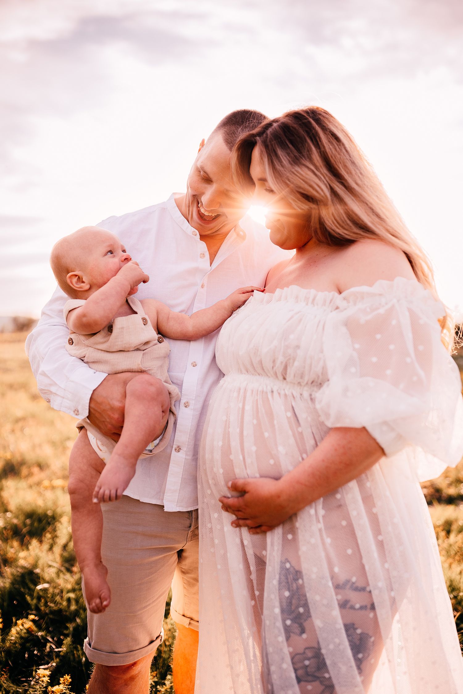 Expecting parents share tender moment with baby during sunset maternity photoshoot.
