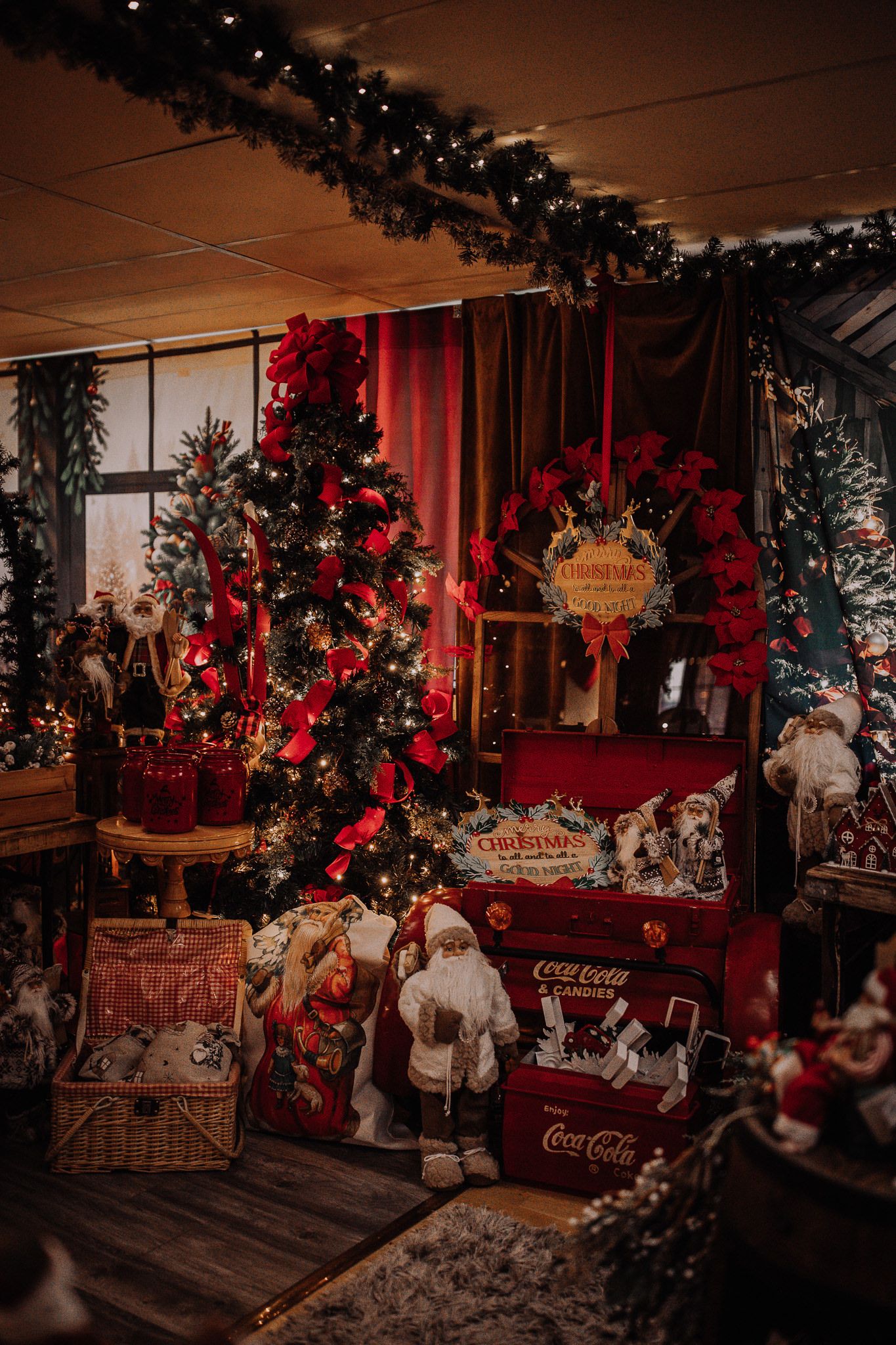 Festive Christmas display with decorated tree, red bows, Santa figurines, and vintage Coca-Cola crates in a cozy holiday setting.