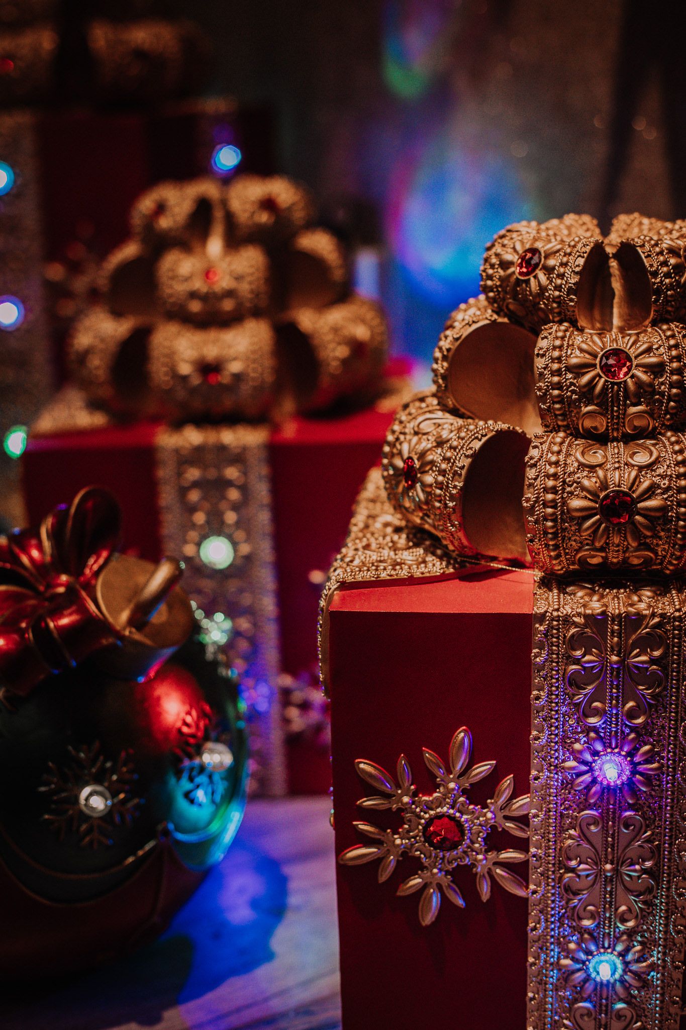 Ornate gift boxes decorated with bows and snowflake designs under colorful Christmas lights.