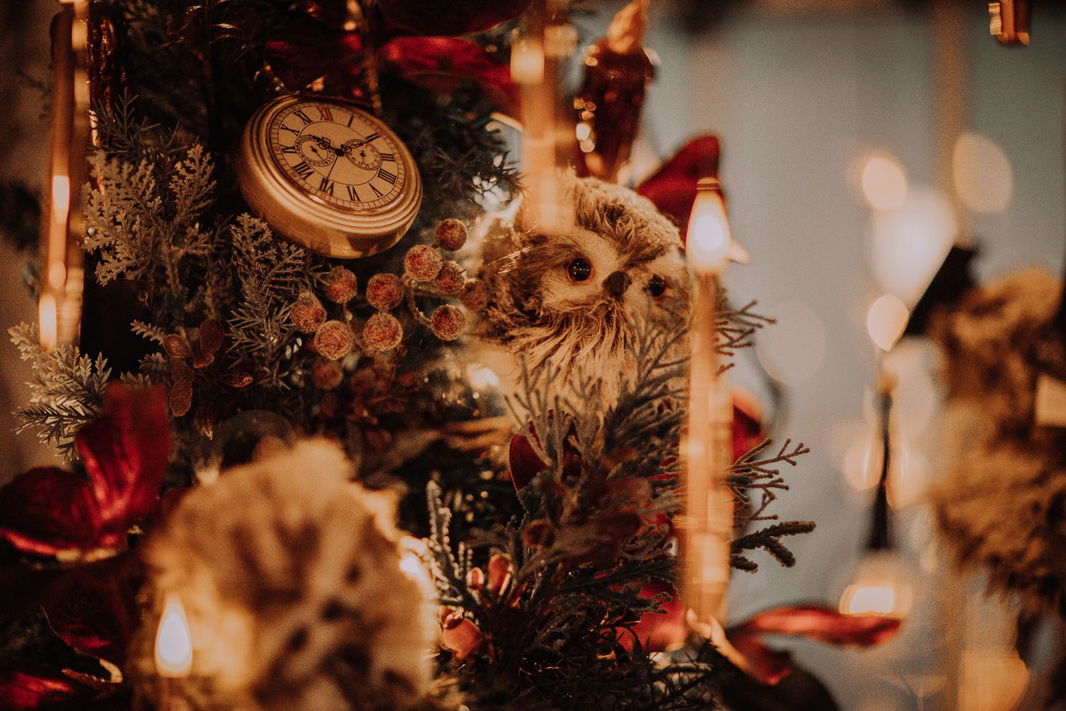 Vintage Christmas tree decorated with owl ornament, clock, red ribbons, and flowers in warm golden bokeh lighting.