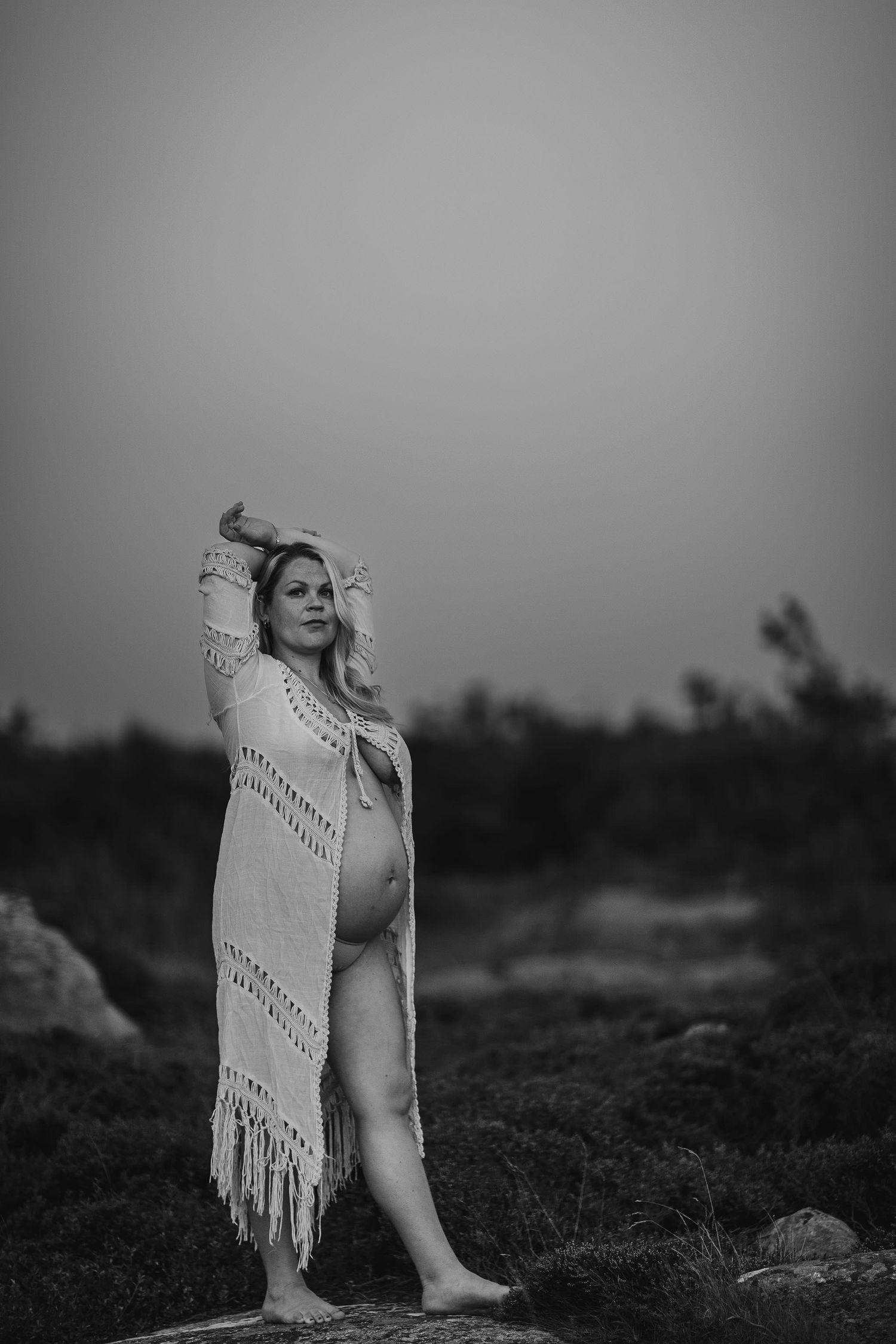 Portrait of a woman wearing a fringed shawl sitting on a hill in black and white.