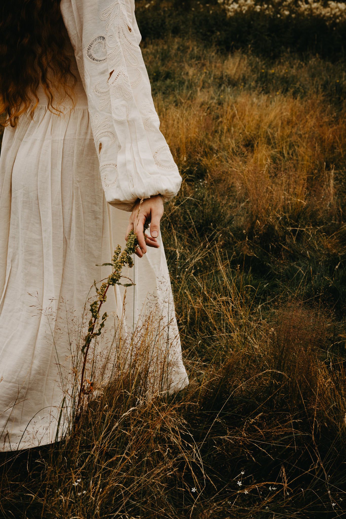 A person in a vintage white dress with billowing sleeves stands in a field of golden autumn grass at sunset.