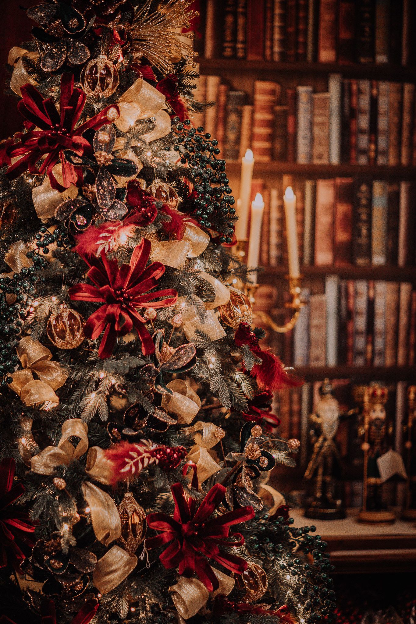 Elegant Christmas tree with red poinsettias, gold ribbons, and warm candlelight against a cozy library backdrop.