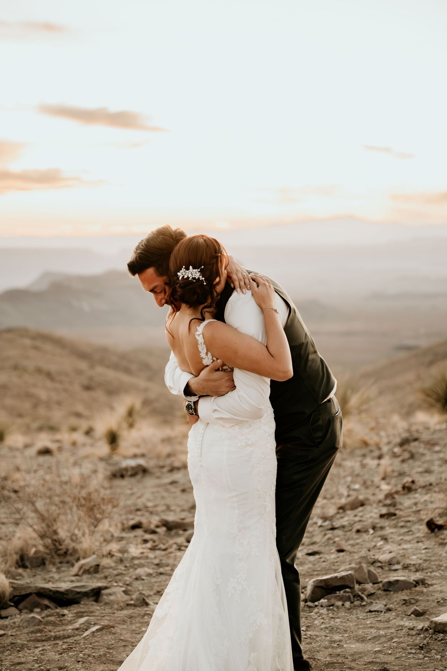 Intimate wedding moment captured against desert mountain backdrop at sunset.