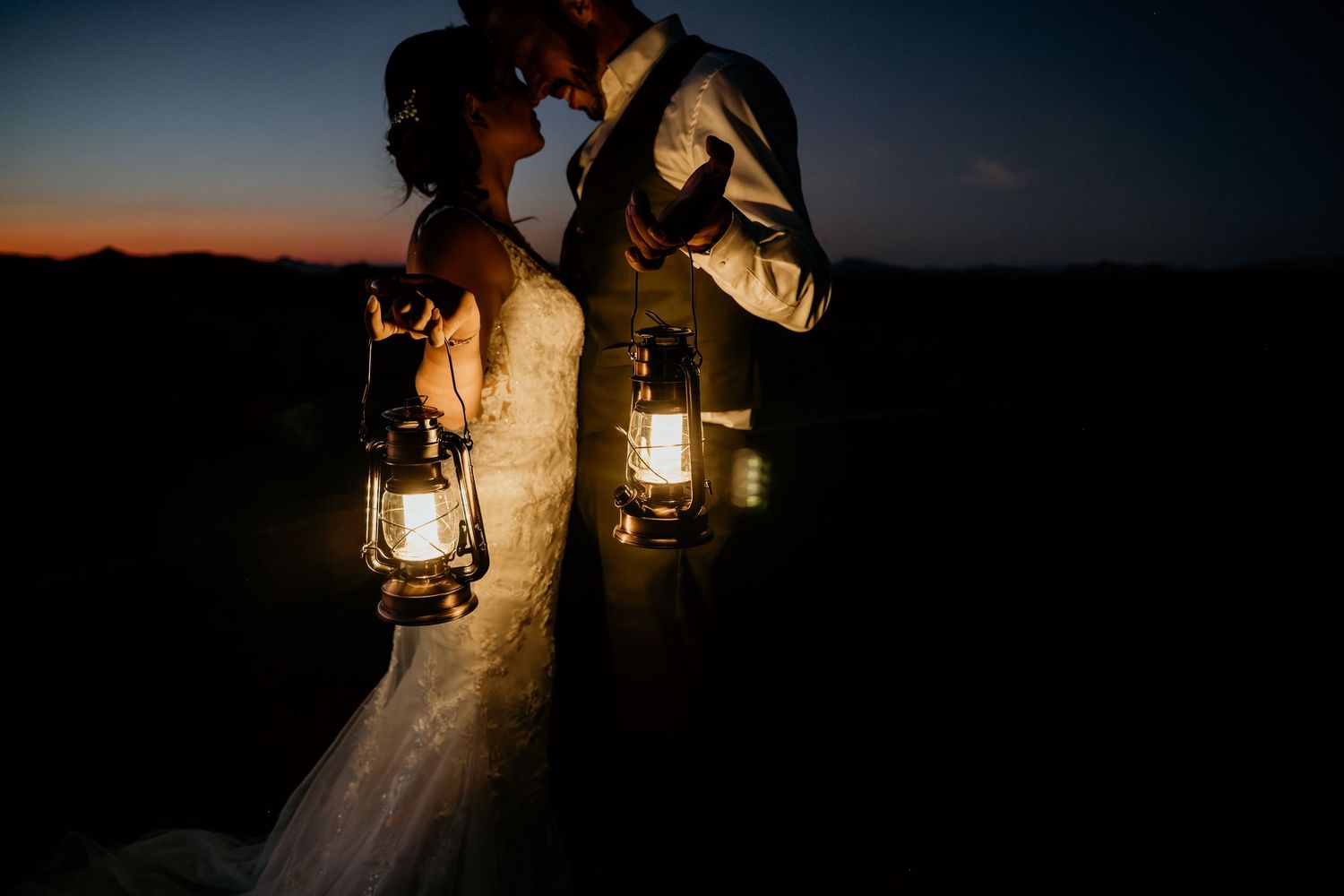 Romantic nighttime wedding photos lit by vintage lanterns against dark sky.