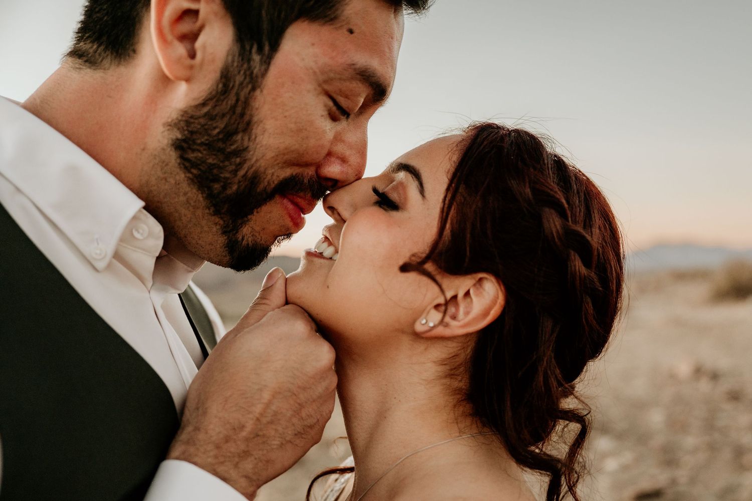 Intimate wedding couple shares romantic moments in a desert setting during sunset.