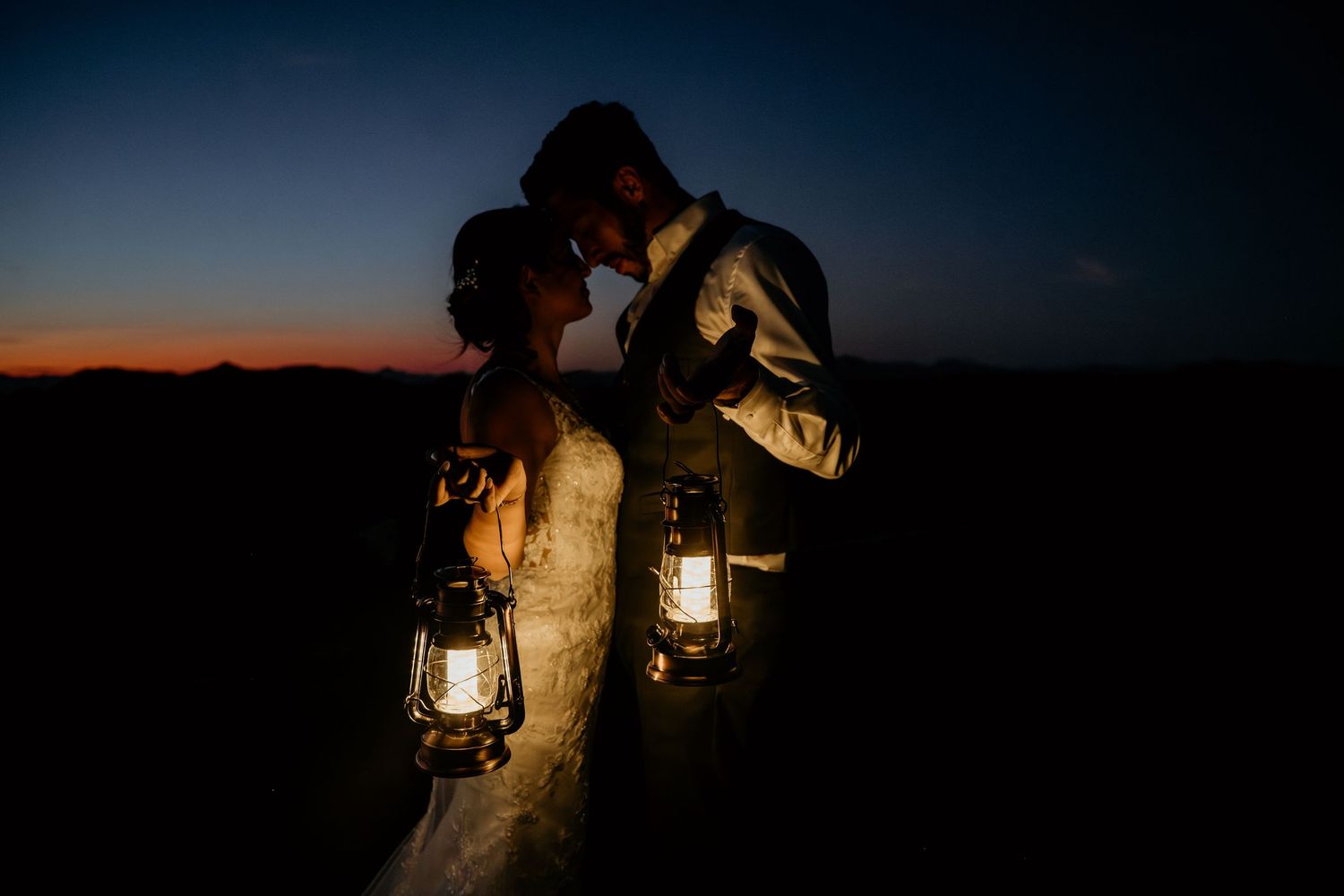 Couple with lanterns creating romantic lighting in the desert at dusk.