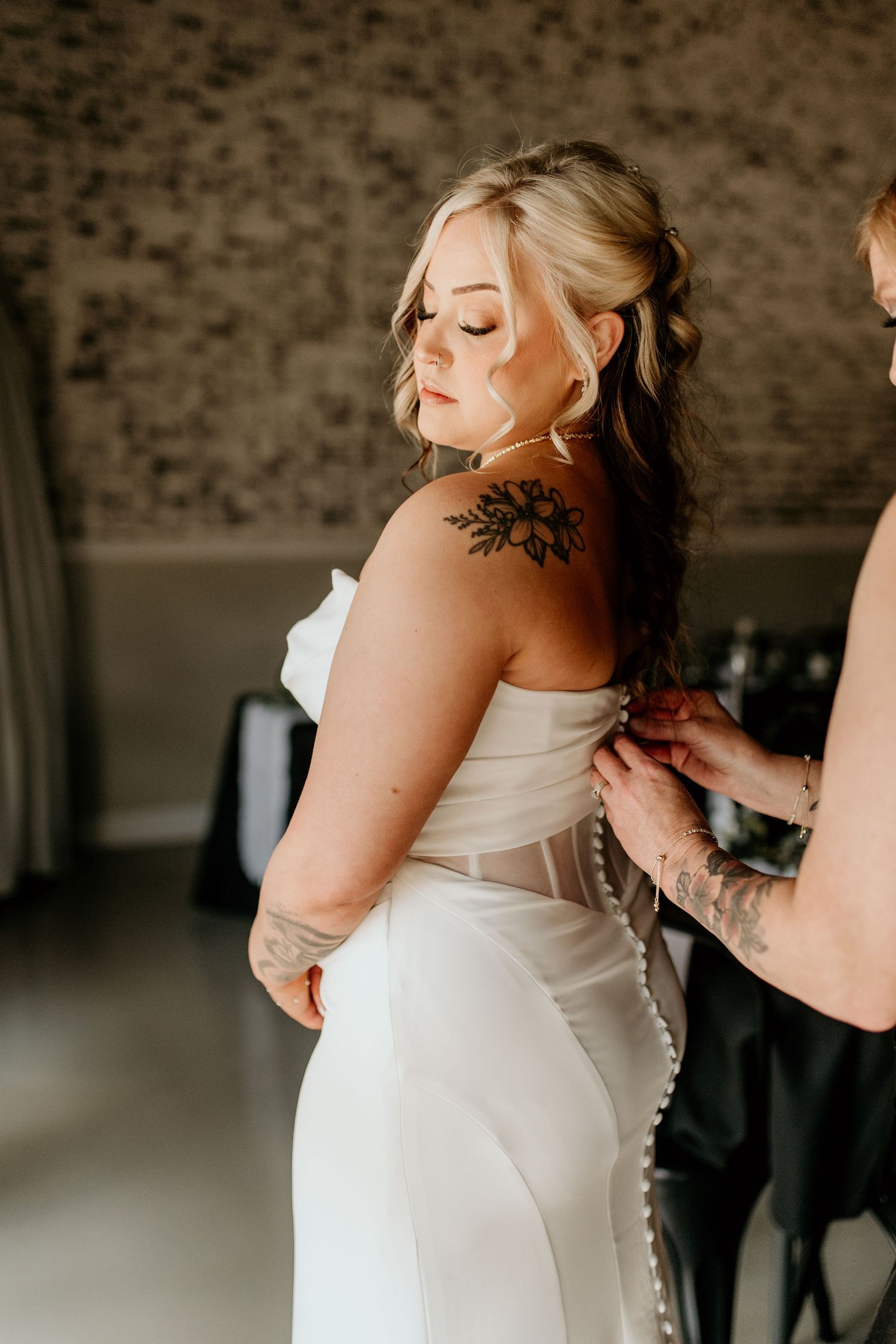 A close-up of a bride's back showing intricate button details and tattoo artwork.