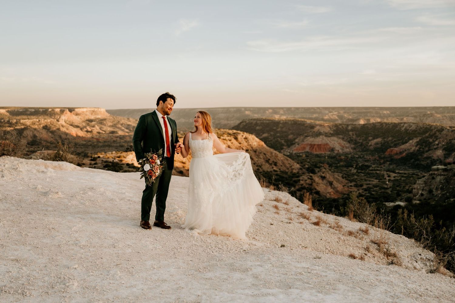 Bride and groom stand on white rock ledge at sunset overlooking Palo Duro Canyon in Texas.