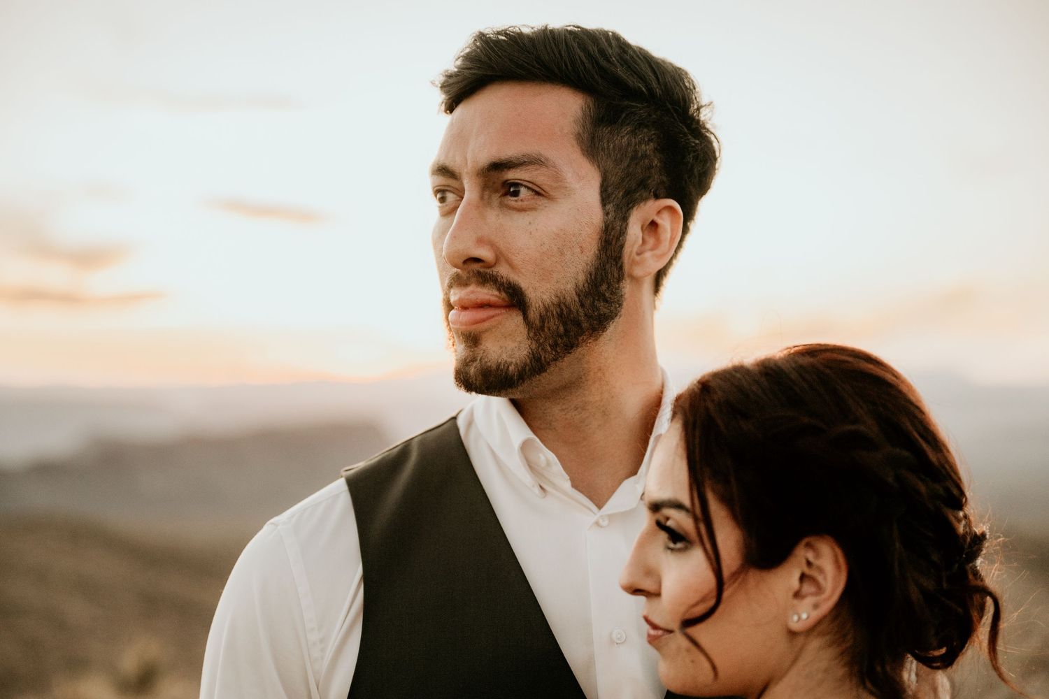 Newlyweds embrace tenderly against a desert mountain backdrop during their wedding photoshoot.