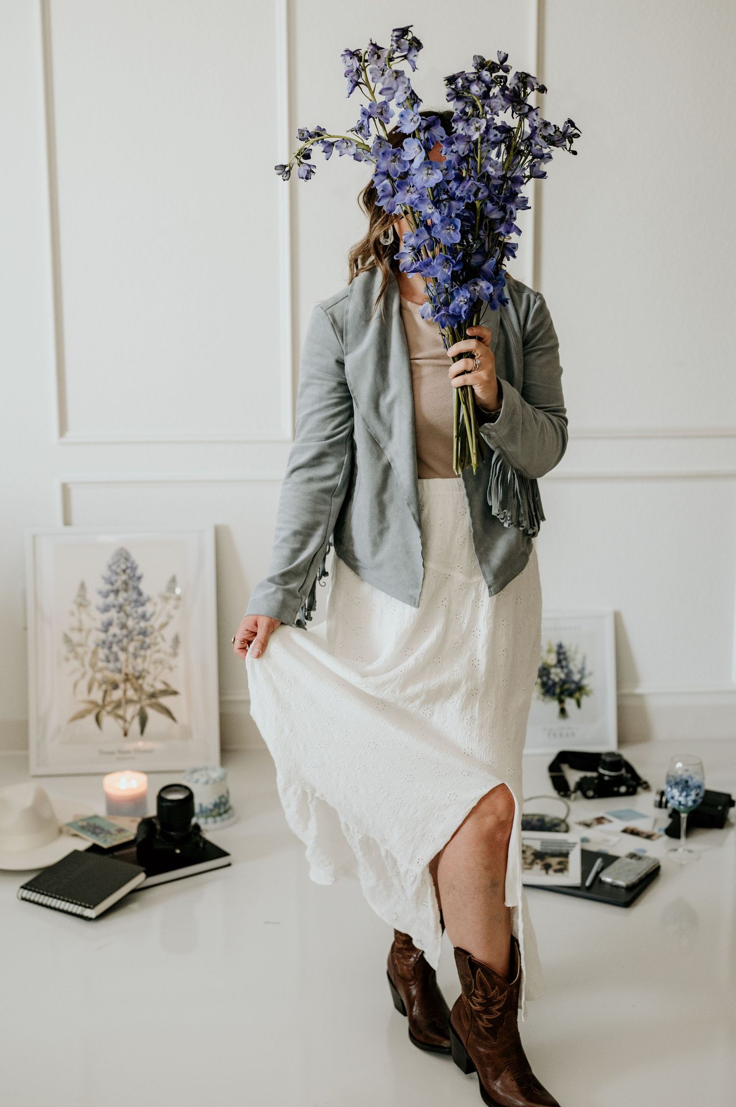 Fashion styling with delphinium flowers, white dress and gray jacket in a minimalist setting.