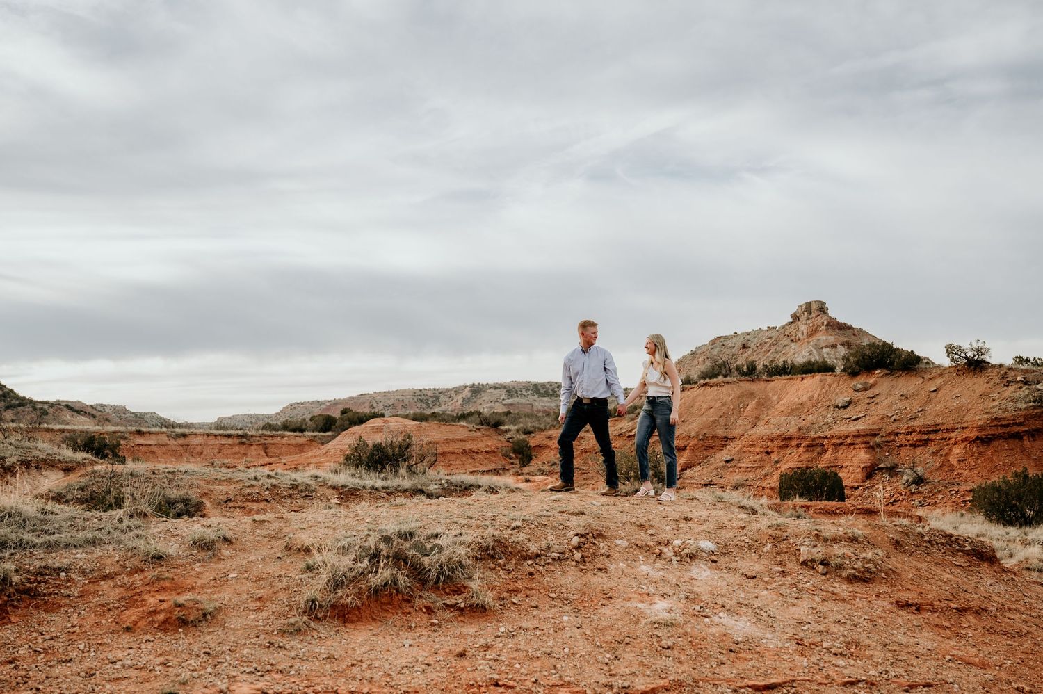Couple holding hands in a red rock desert landscape under cloudy skies in the American Southwest.
