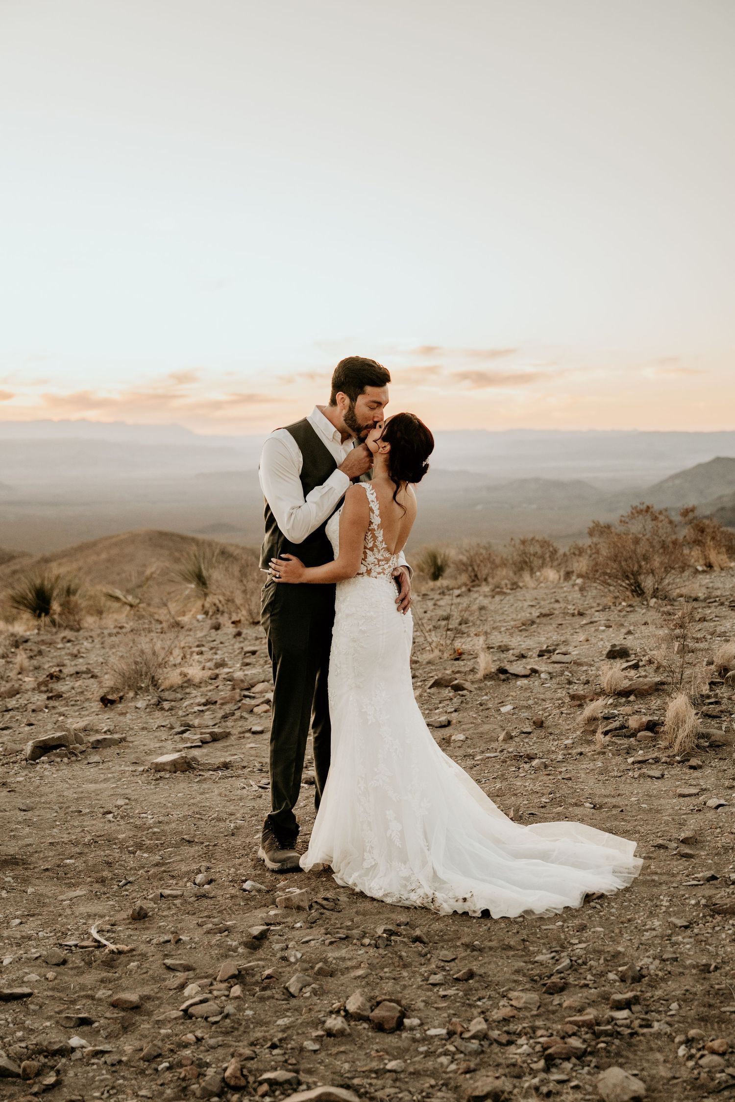 Wedding couple shares romantic moments on a desert mountain overlook during sunset.