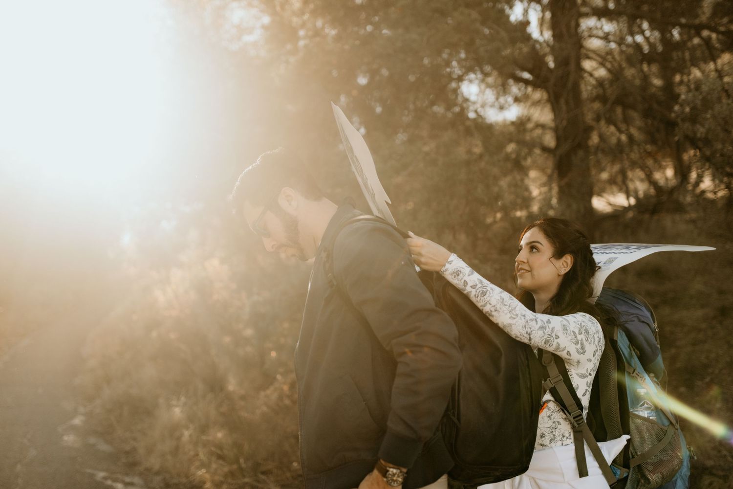 A couple shares a romantic kiss in a sunlit forest during their wedding photo session.