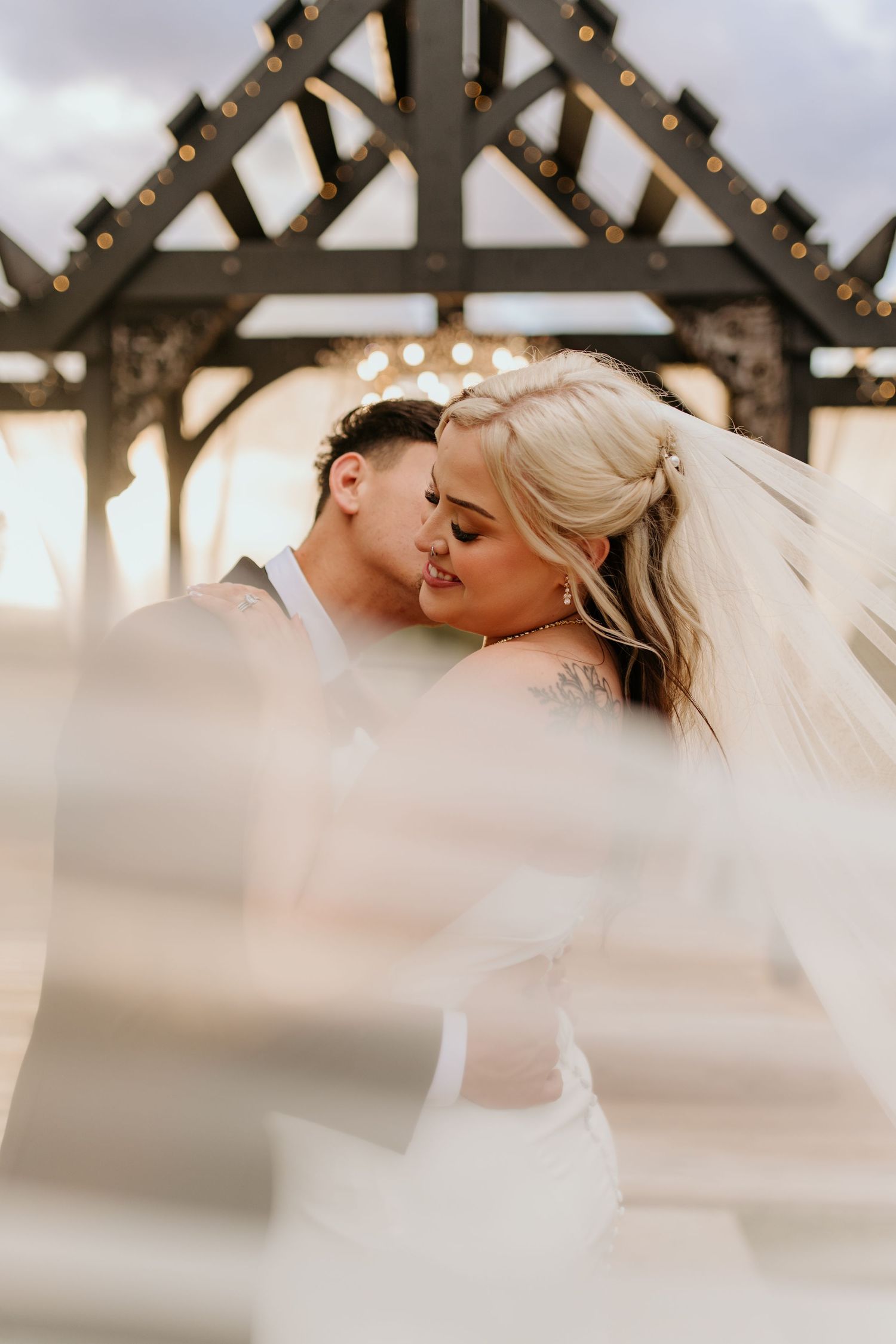 Romantic wedding scene under a wooden pergola decorated with string lights.