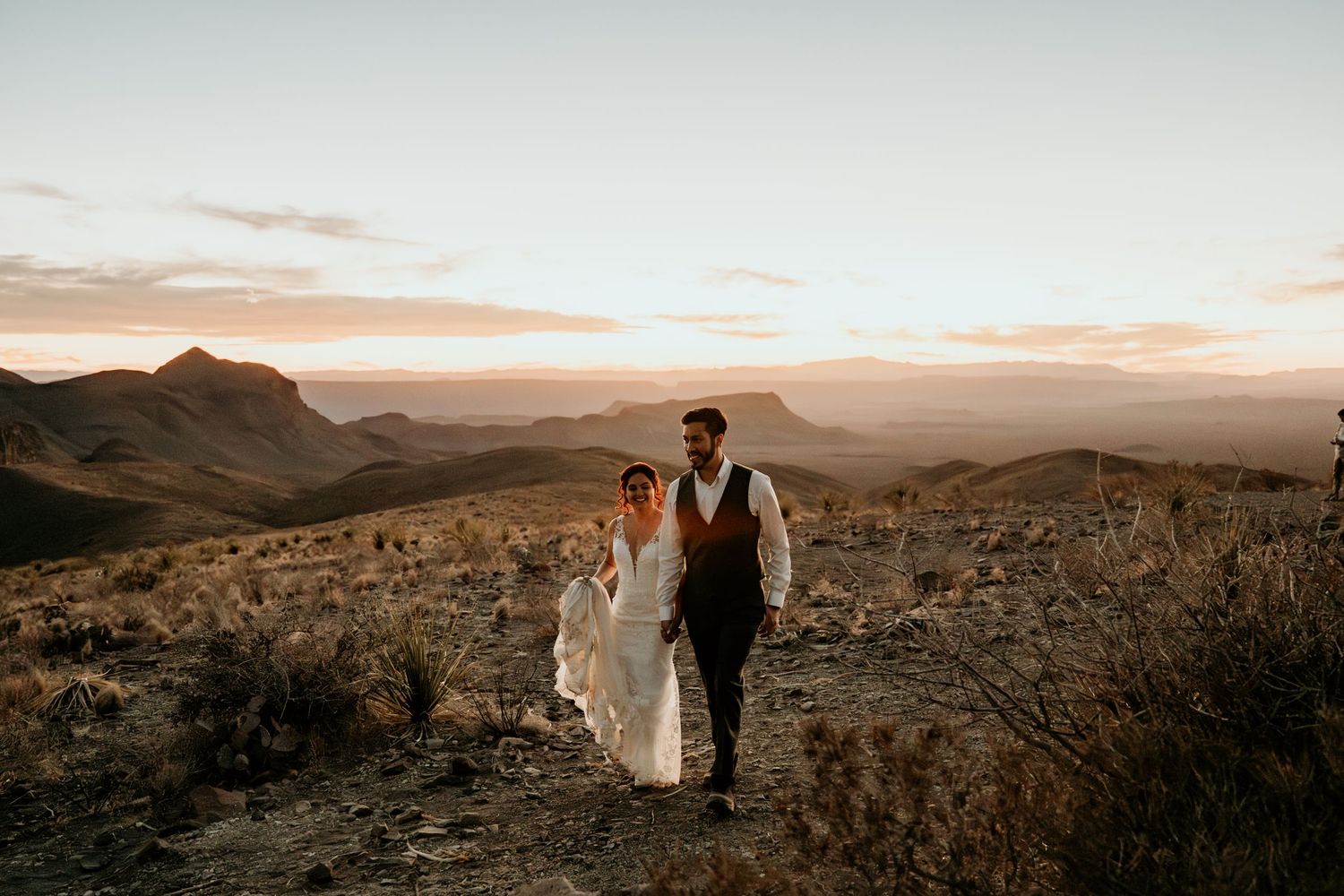 Wedding couple walking along desert mountain ridge during golden hour.