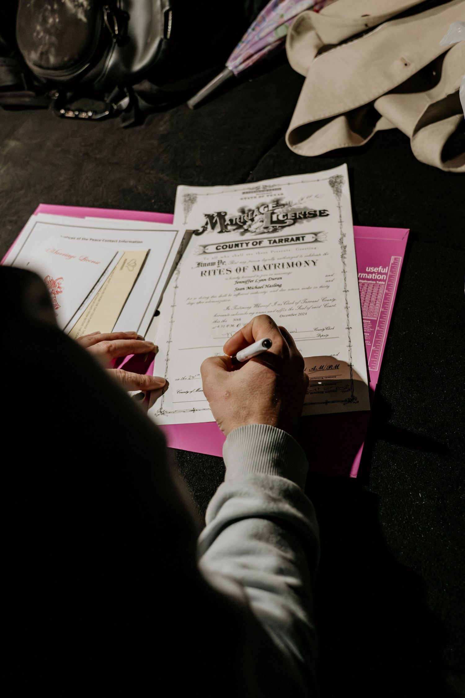 Wedding documents and paperwork being signed on a dark table.