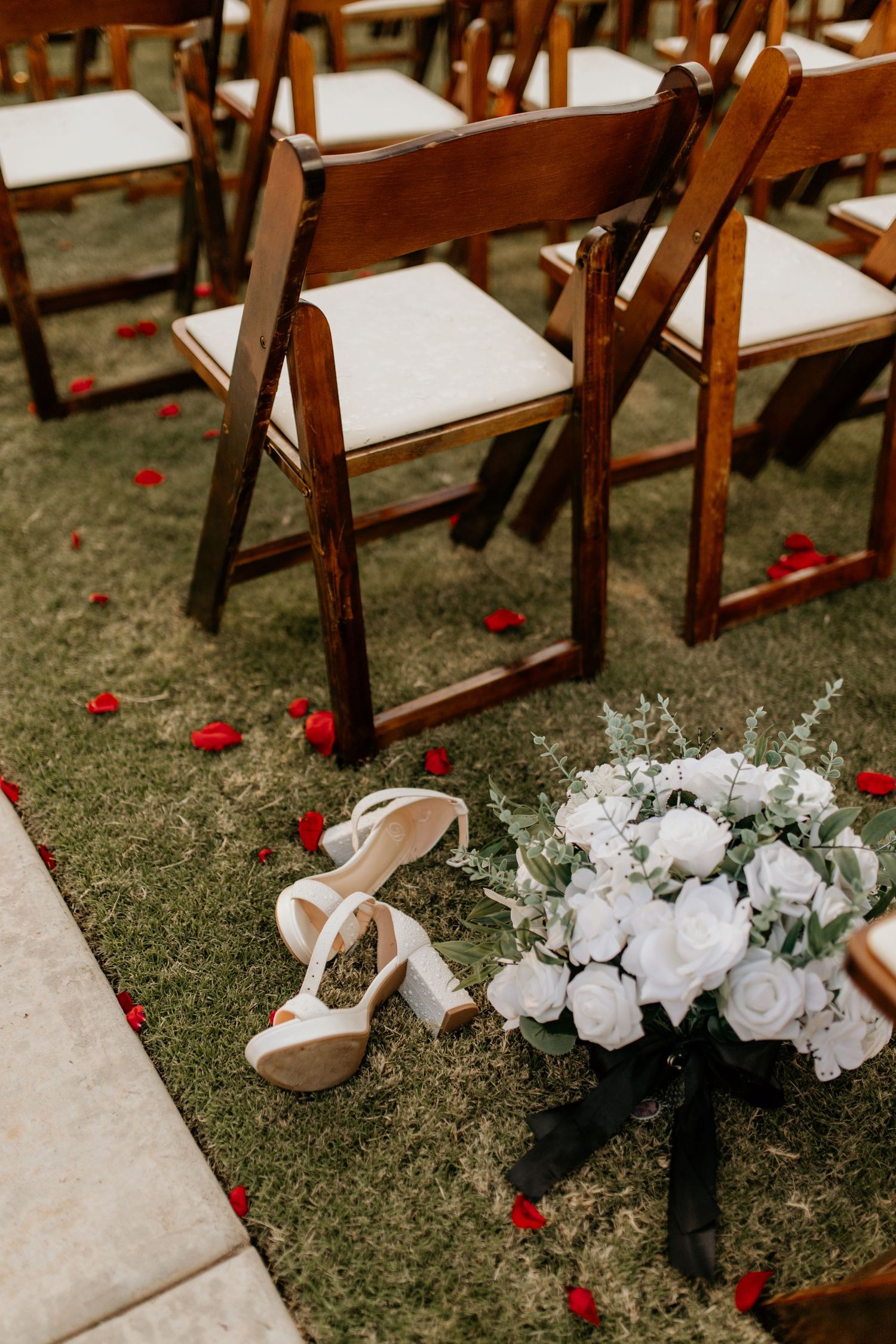Wooden folding chairs and white floral arrangements set up for an outdoor wedding ceremony.