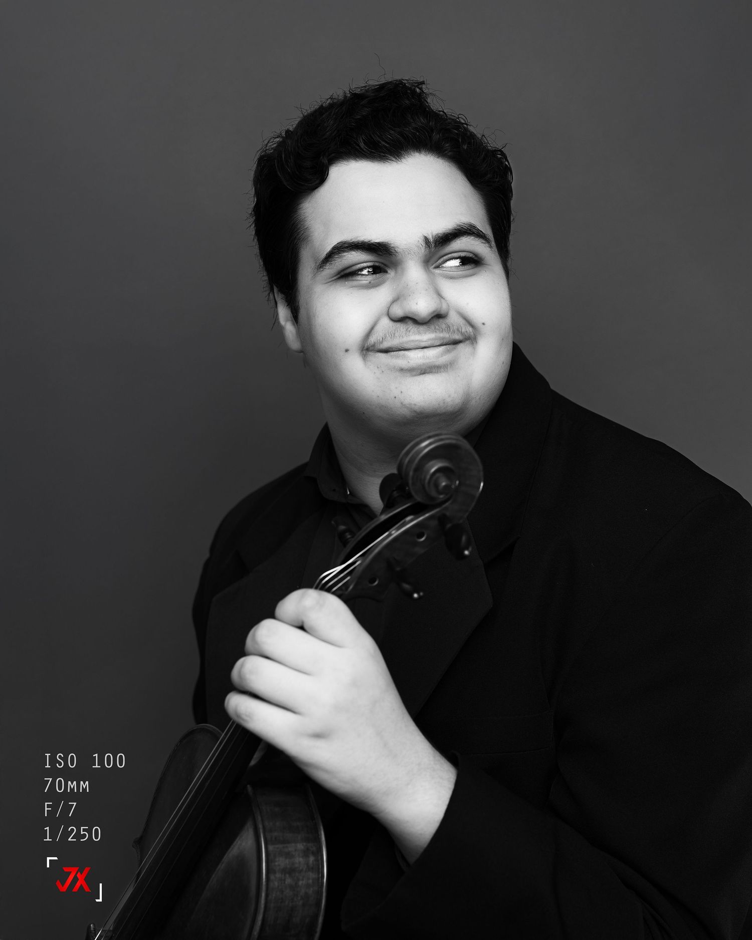 Young male musician smiling warmly while holding a violin, captured in elegant black and white portrait photography.
