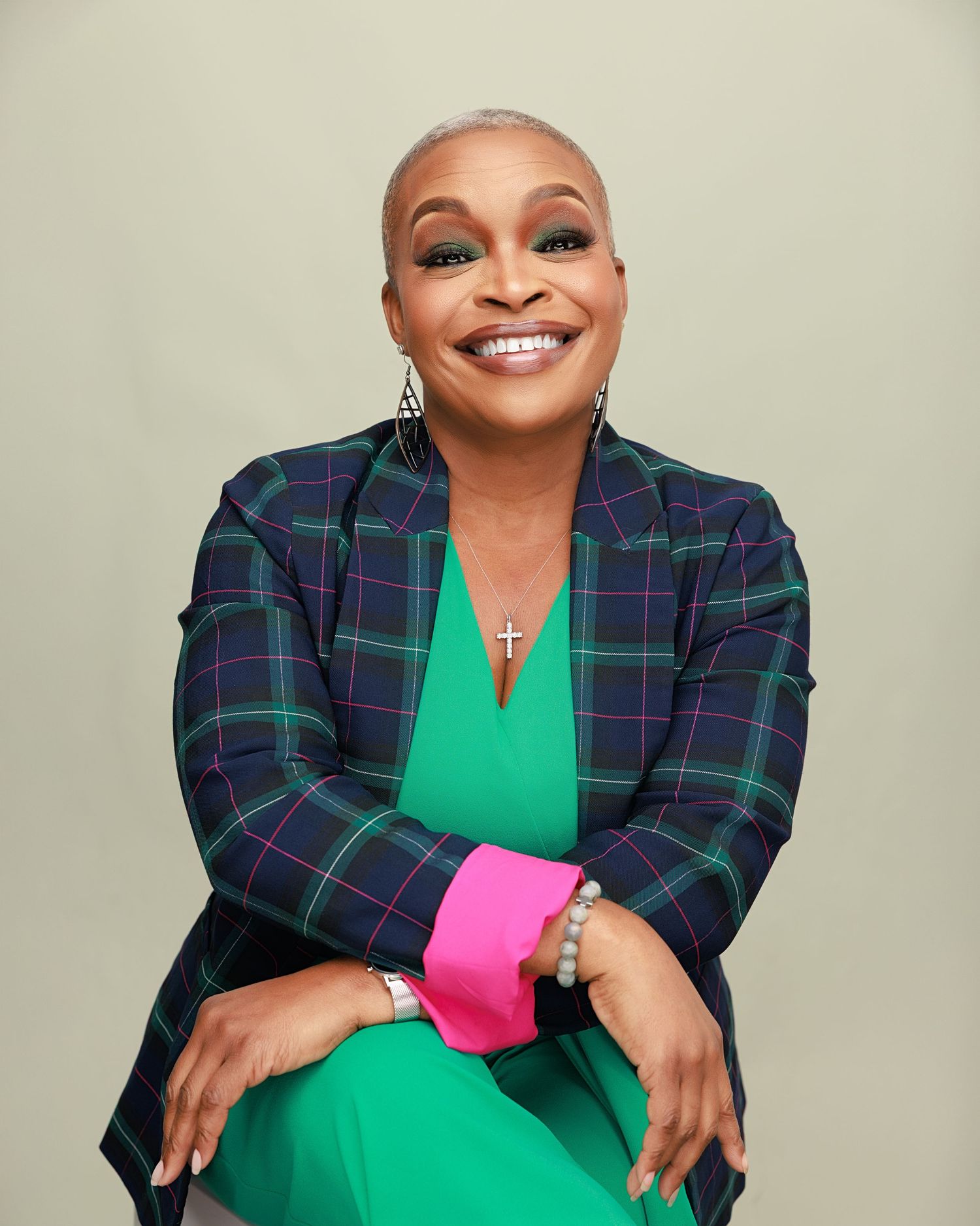 Professional portrait of someone wearing a navy plaid blazer and bright green dress against neutral background.
