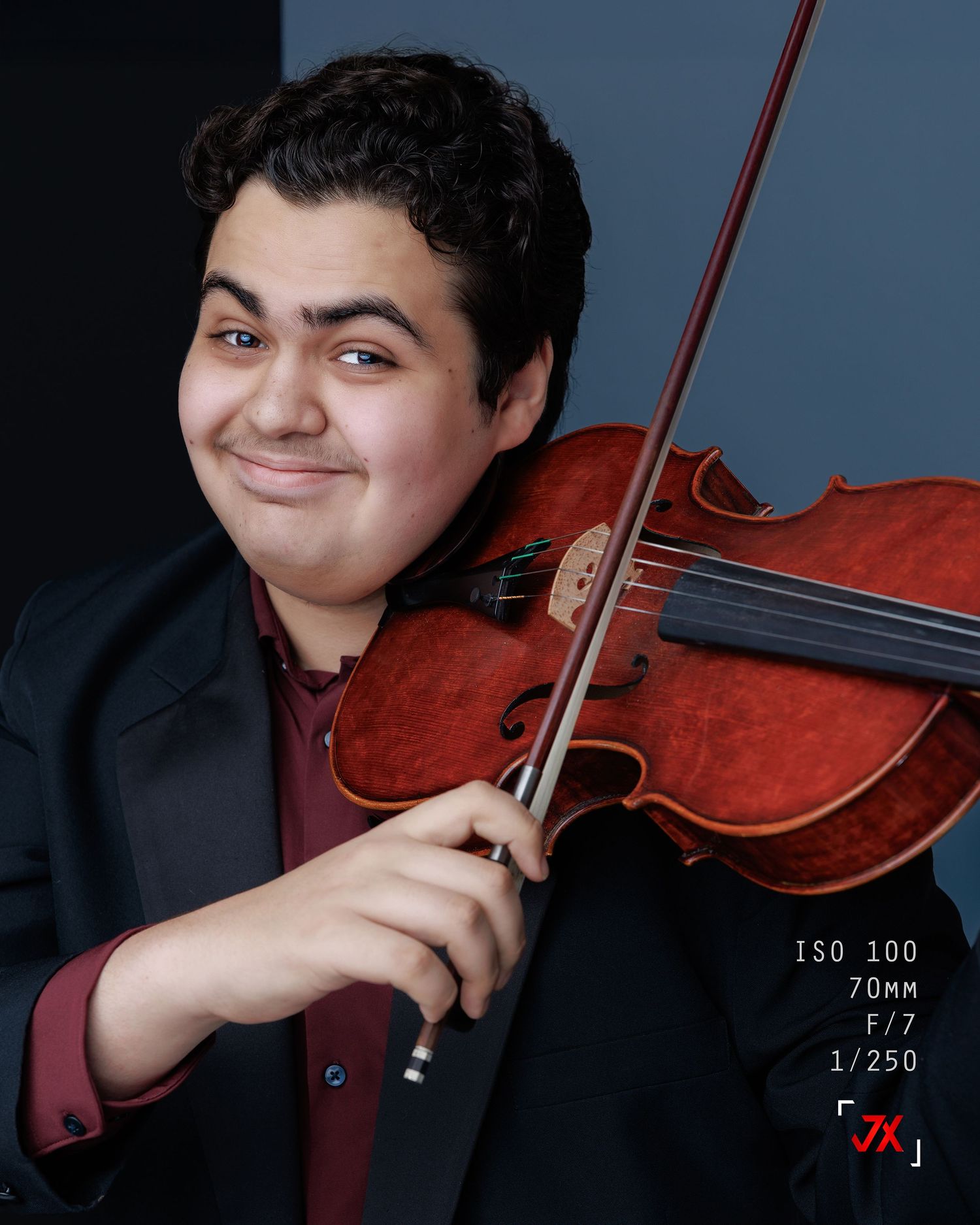 Young male violinist in a dark blazer smiling while playing violin, professional portrait photo.