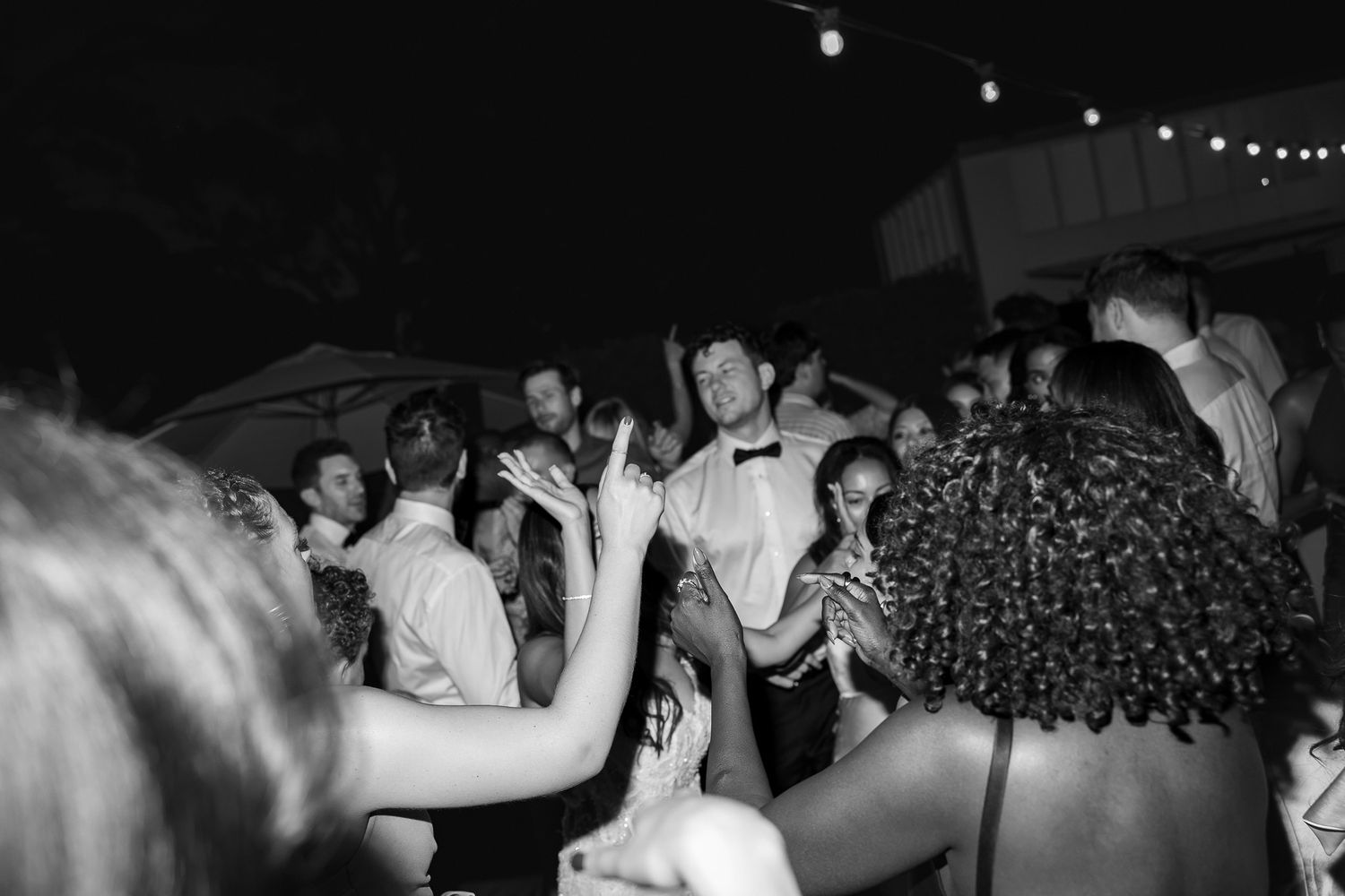 Black and white photo of wedding guests dancing together on a crowded outdoor dance floor at night.