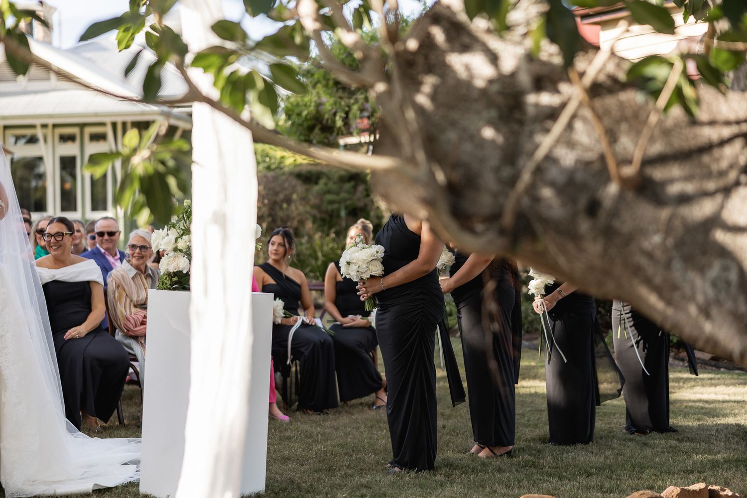 Bridesmaids in black dresses walking down the aisle at an outdoor wedding ceremony.