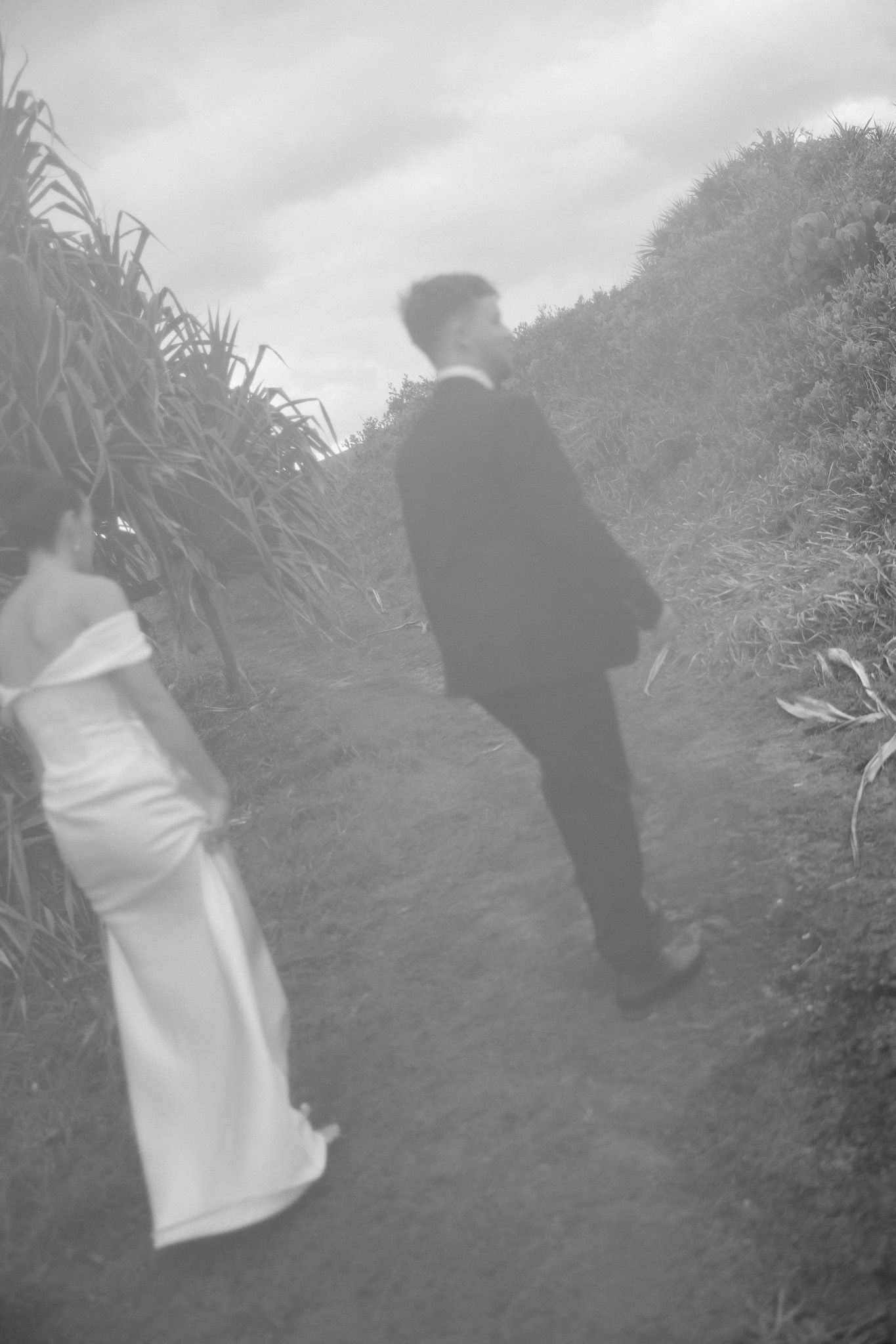 Black and white photo of bride and groom walking along narrow garden path after ceremony.