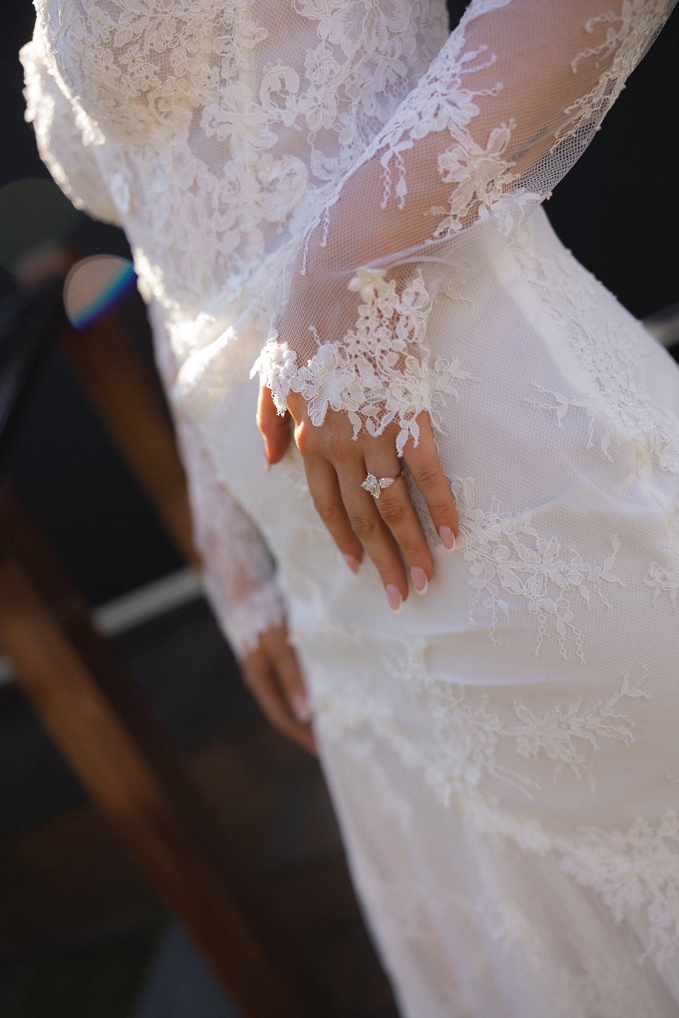 Bride in lace wedding gown with long sleeves displaying diamond engagement ring on her hand.