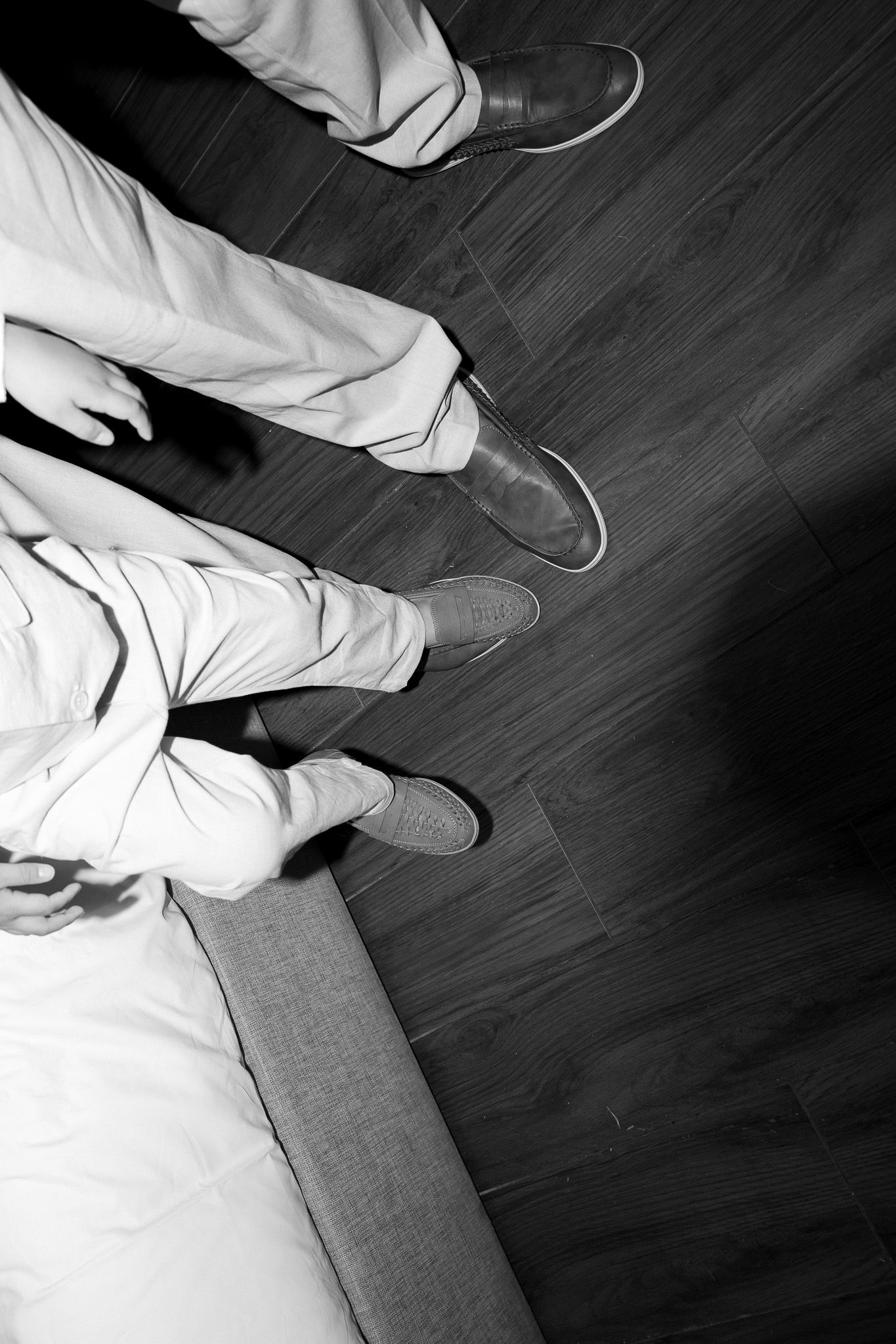Black and white overhead view of two people standing in dress shoes on wooden floor.