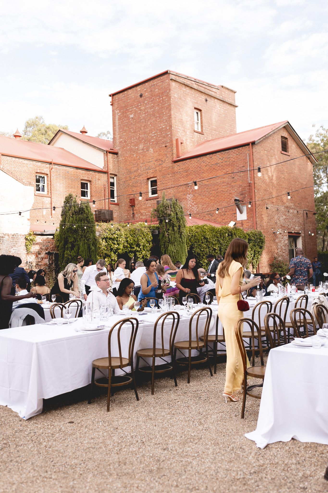 Guests dining at outdoor wedding reception beside rustic red brick venue.