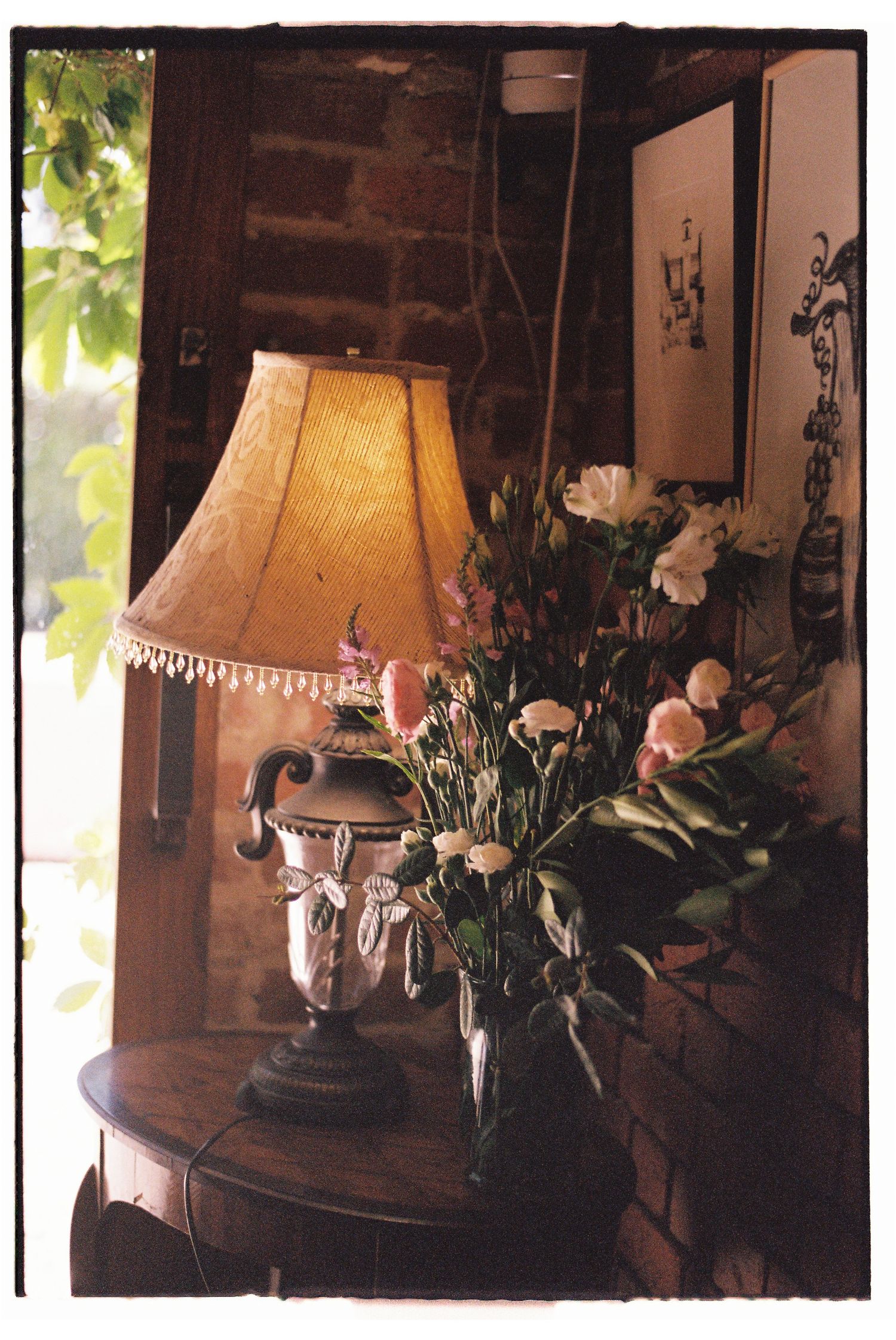 Vintage table lamp with fringe shade beside a floral arrangement on an antique wooden side table in a rustic interior.