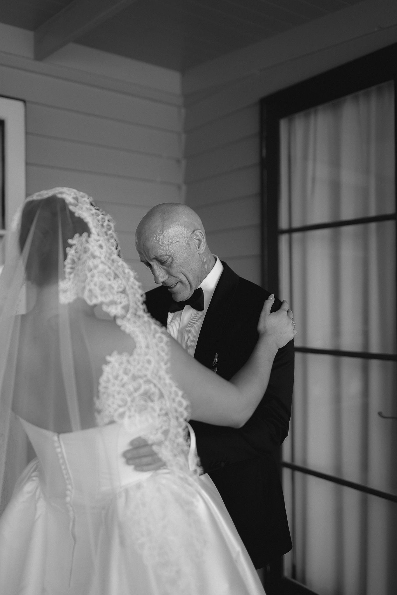 Emotional black and white photo of father embracing bride in wedding dress before ceremony.