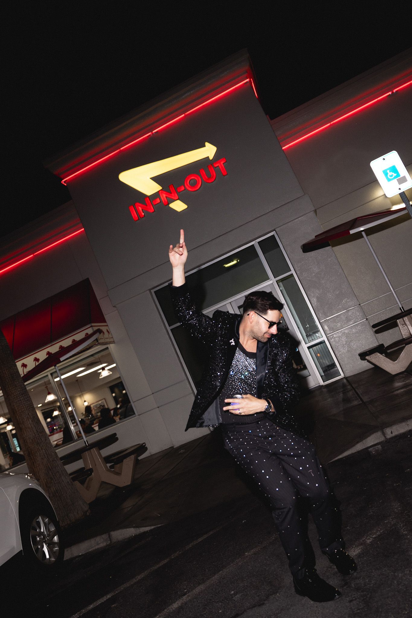 Man in sparkly black suit striking a pose outside In-N-Out Burger restaurant at night.