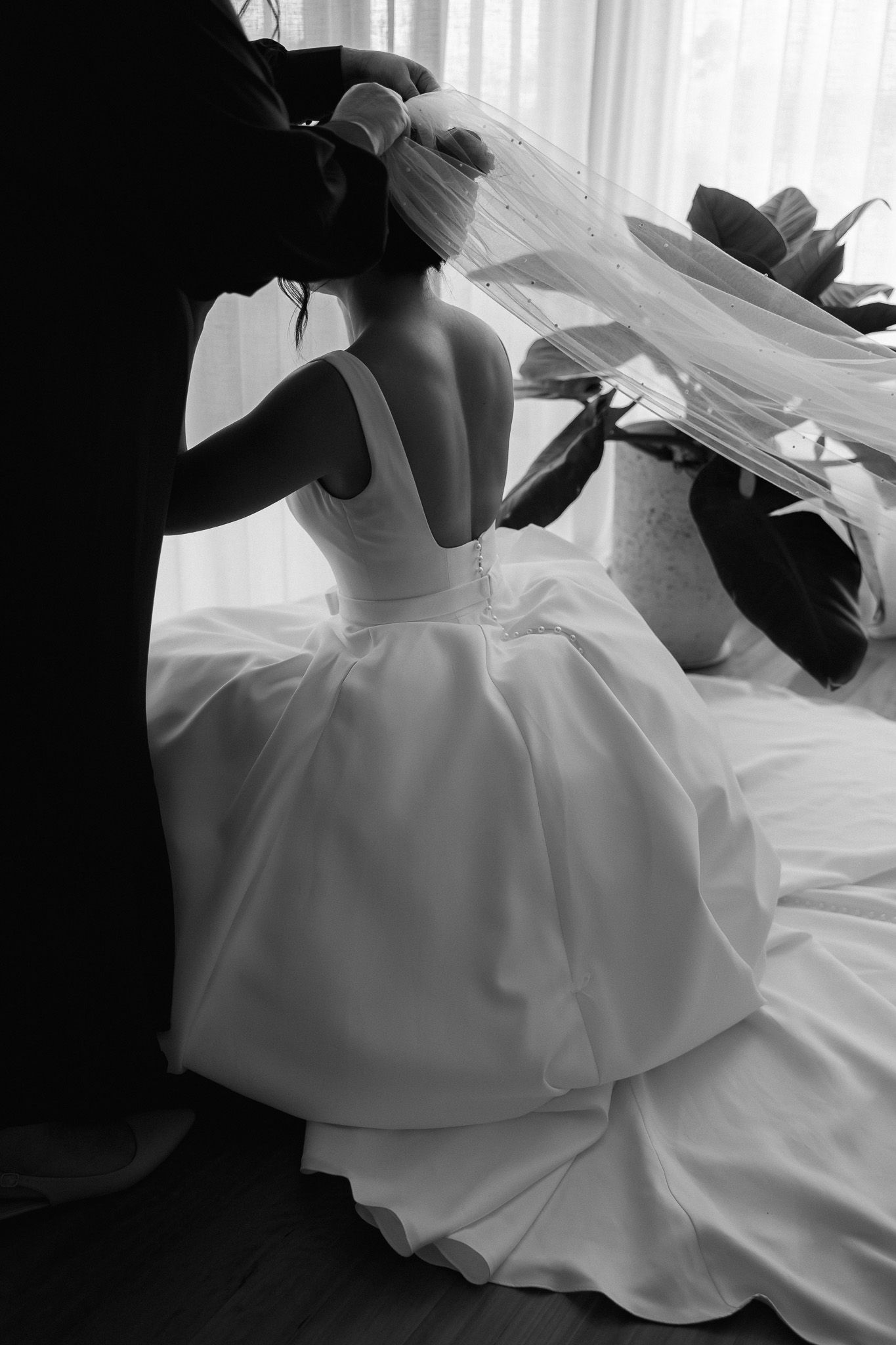 Black and white image of bride having veil placed on her head before wedding.