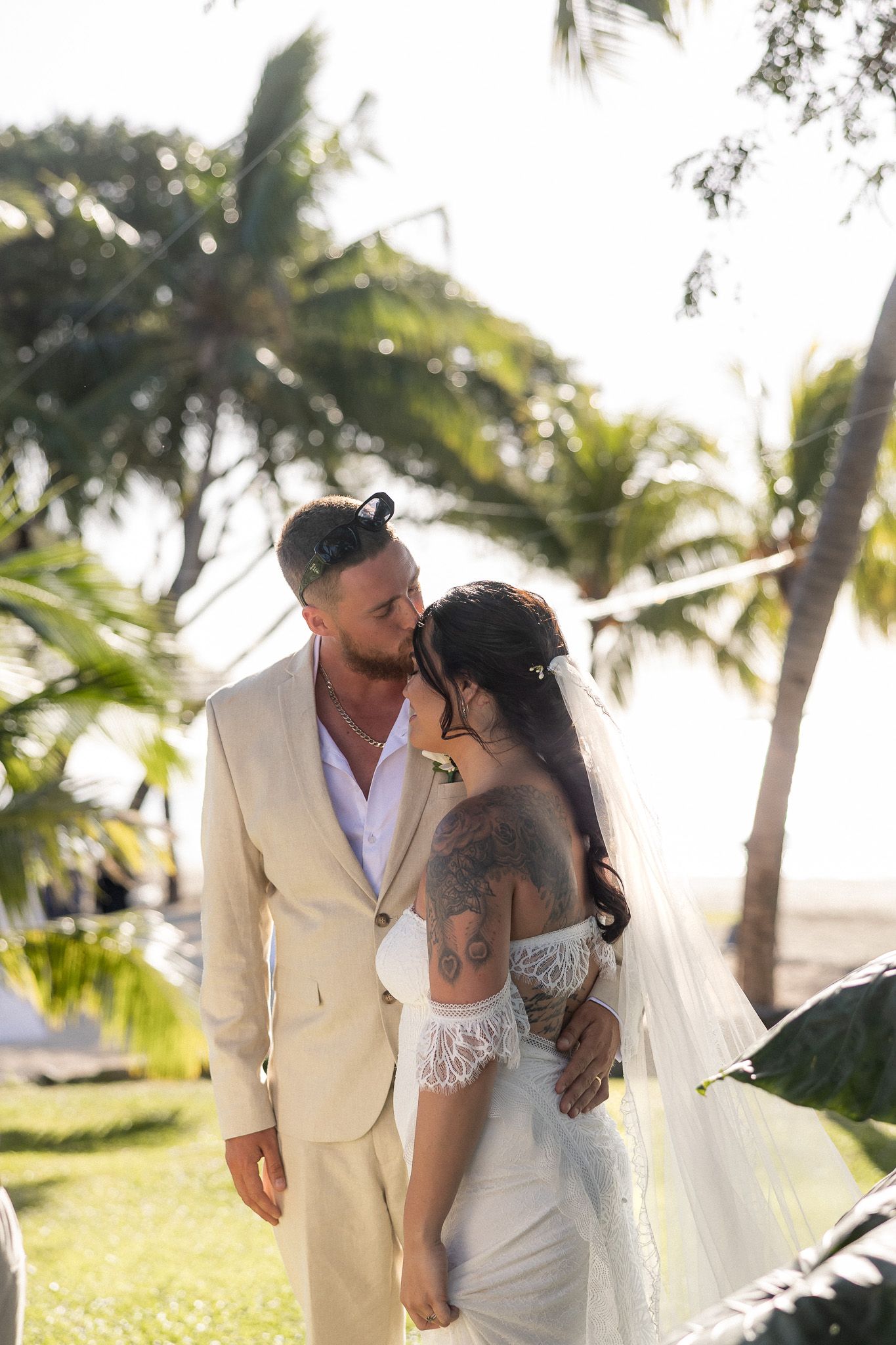 Bride and groom share a romantic moment surrounded by tropical palm trees at a beach wedding.