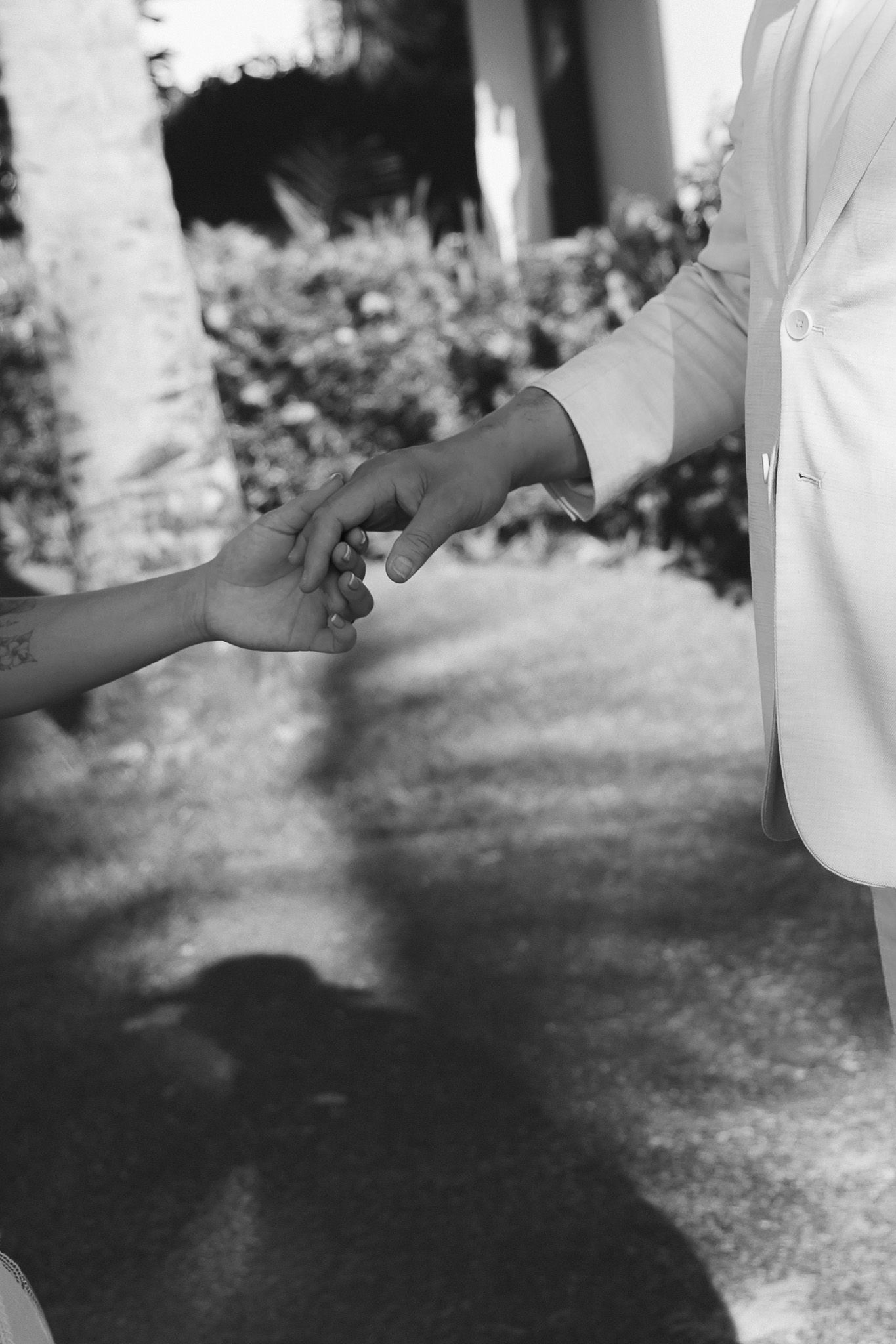 Black and white photo of bride and groom holding hands outdoors on wedding day.