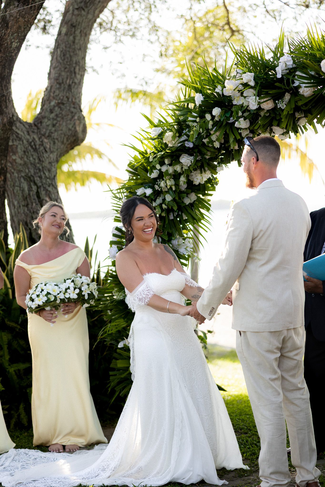 Bride and groom exchanging vows under floral arch at outdoor tropical wedding ceremony.