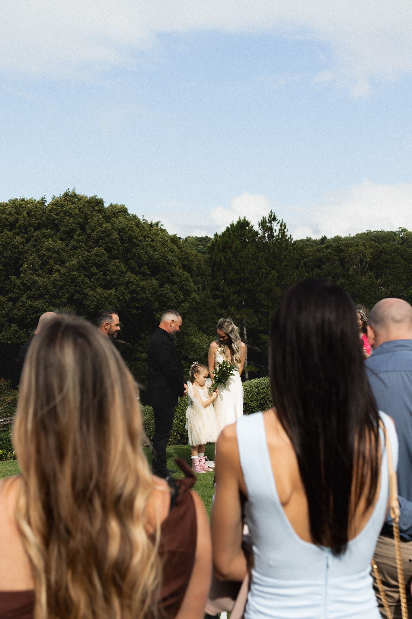Wedding guests watching bride and groom exchange vows at outdoor garden ceremony.
