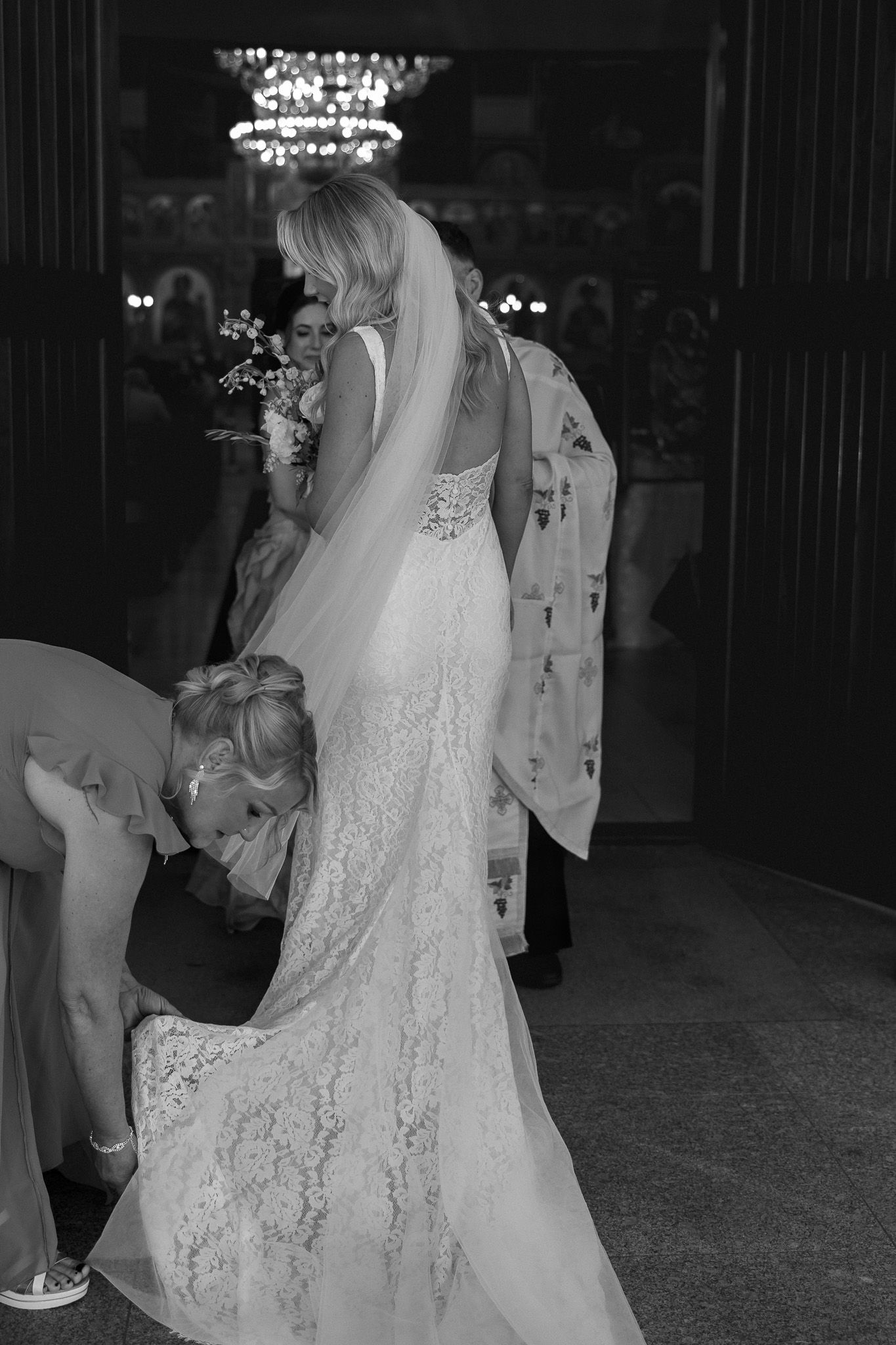 Black and white photo of a bridesmaid adjusting the lace train of a brides wedding gown.